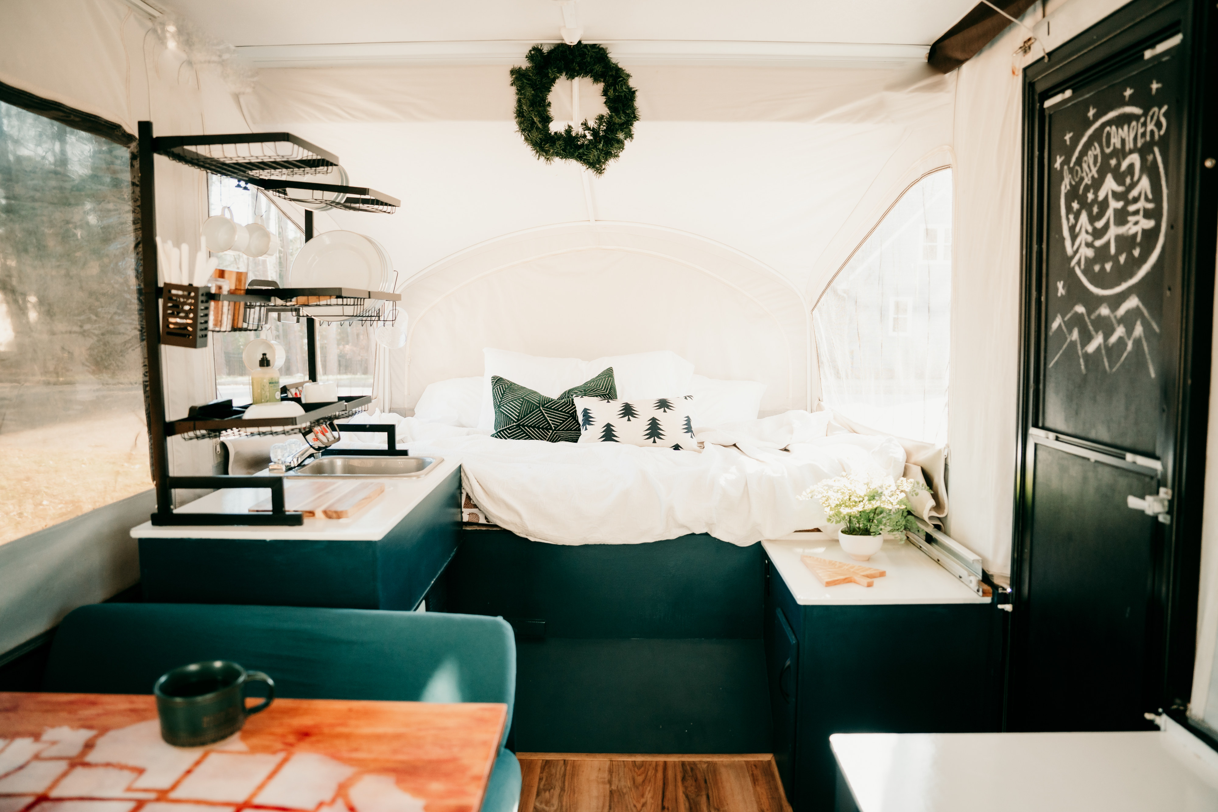 Cozy RV rental interior featuring a comfy bed, compact kitchen with sink, and a "Happy Campers" chalkboard door.. Jayco Jay 2015