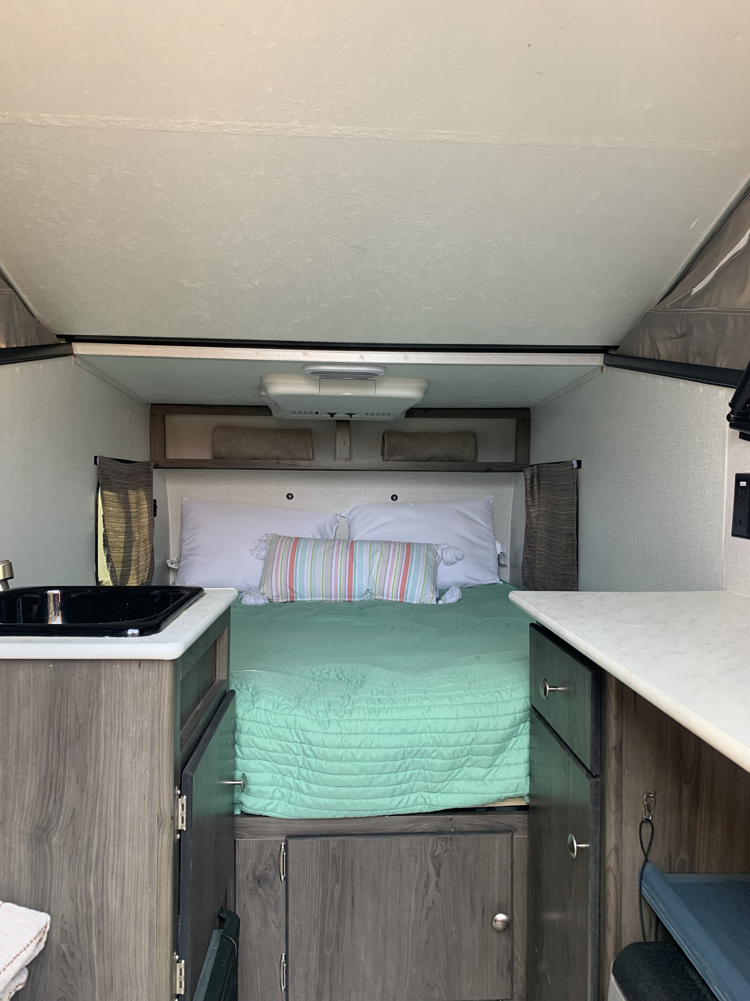 Cozy RV rental interior: a compact bed with green quilt, small sink, and counter, ideal for travel adventures.. Forest River Viking TD 2022