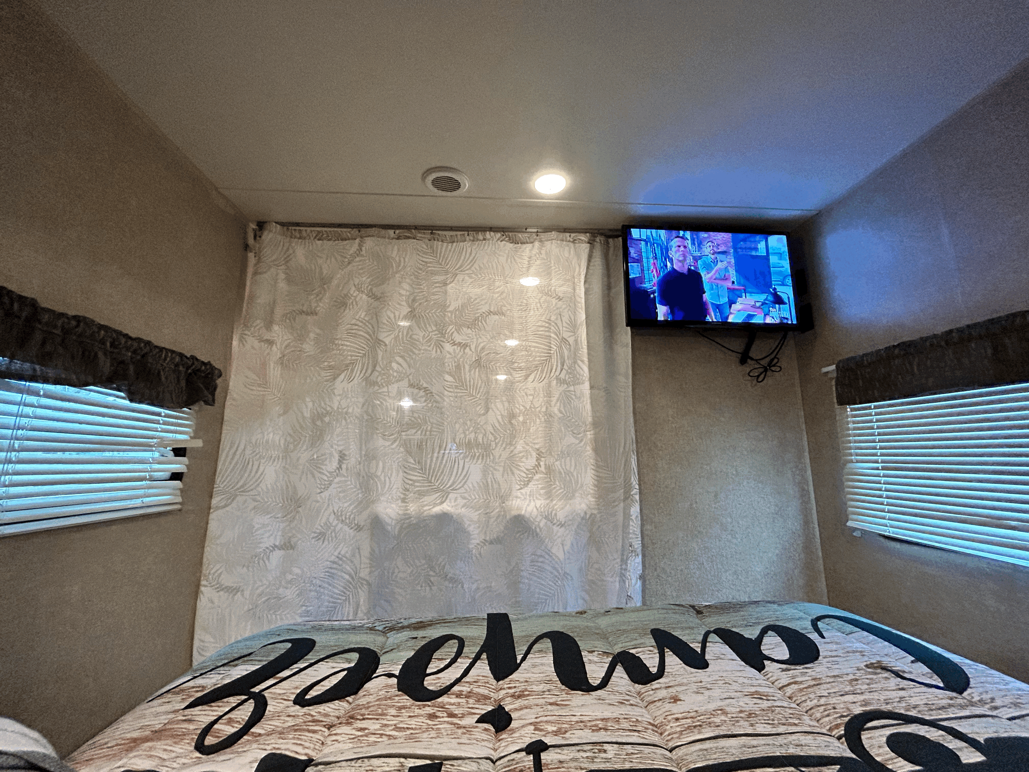 Inside an **RV rental**: a compact bedroom with a TV, window blinds, and a privacy curtain featuring palm leaves.. Coachmen Other 2017