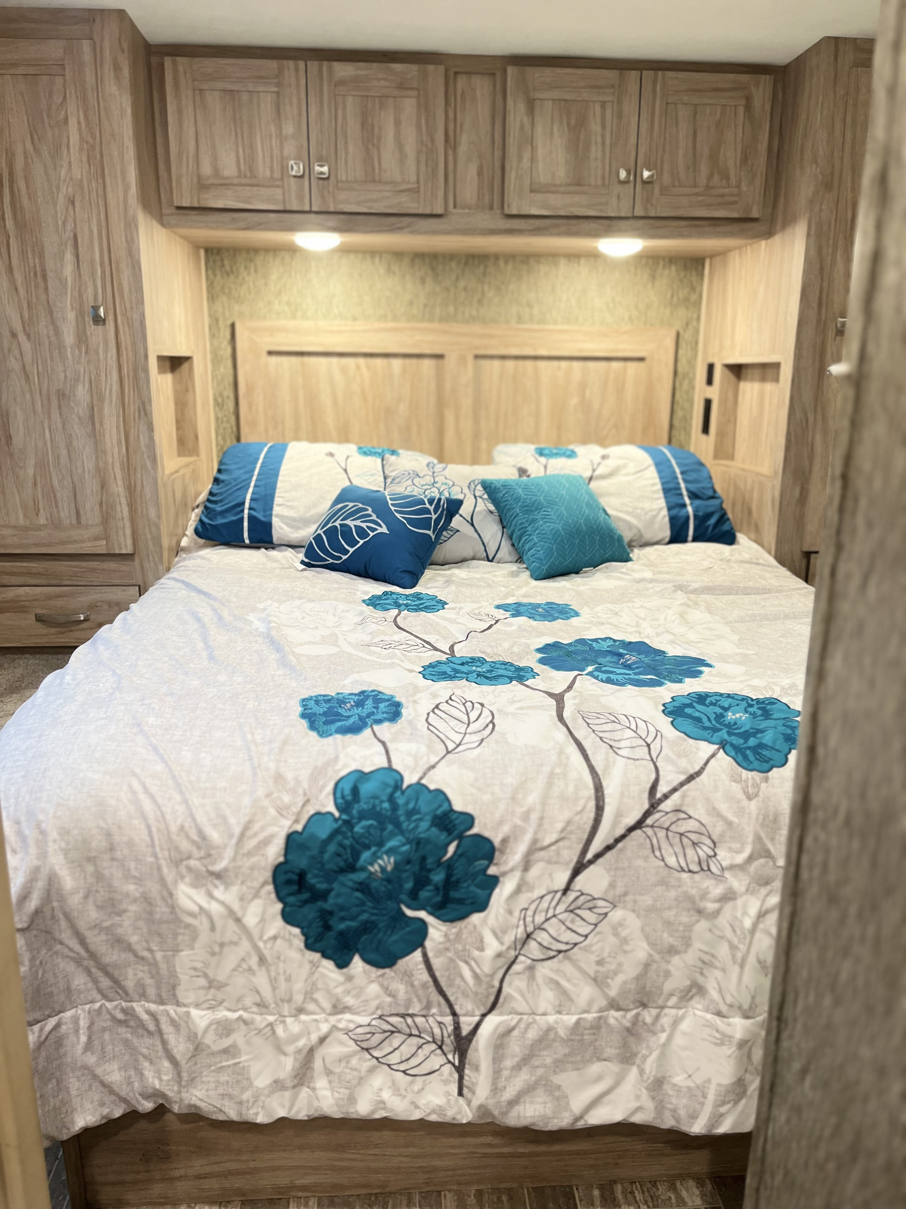 Cozy RV rental bedroom featuring vibrant teal floral bedding, practical overhead wooden storage, and warm lighting.. Forest River Sunseeker 2019