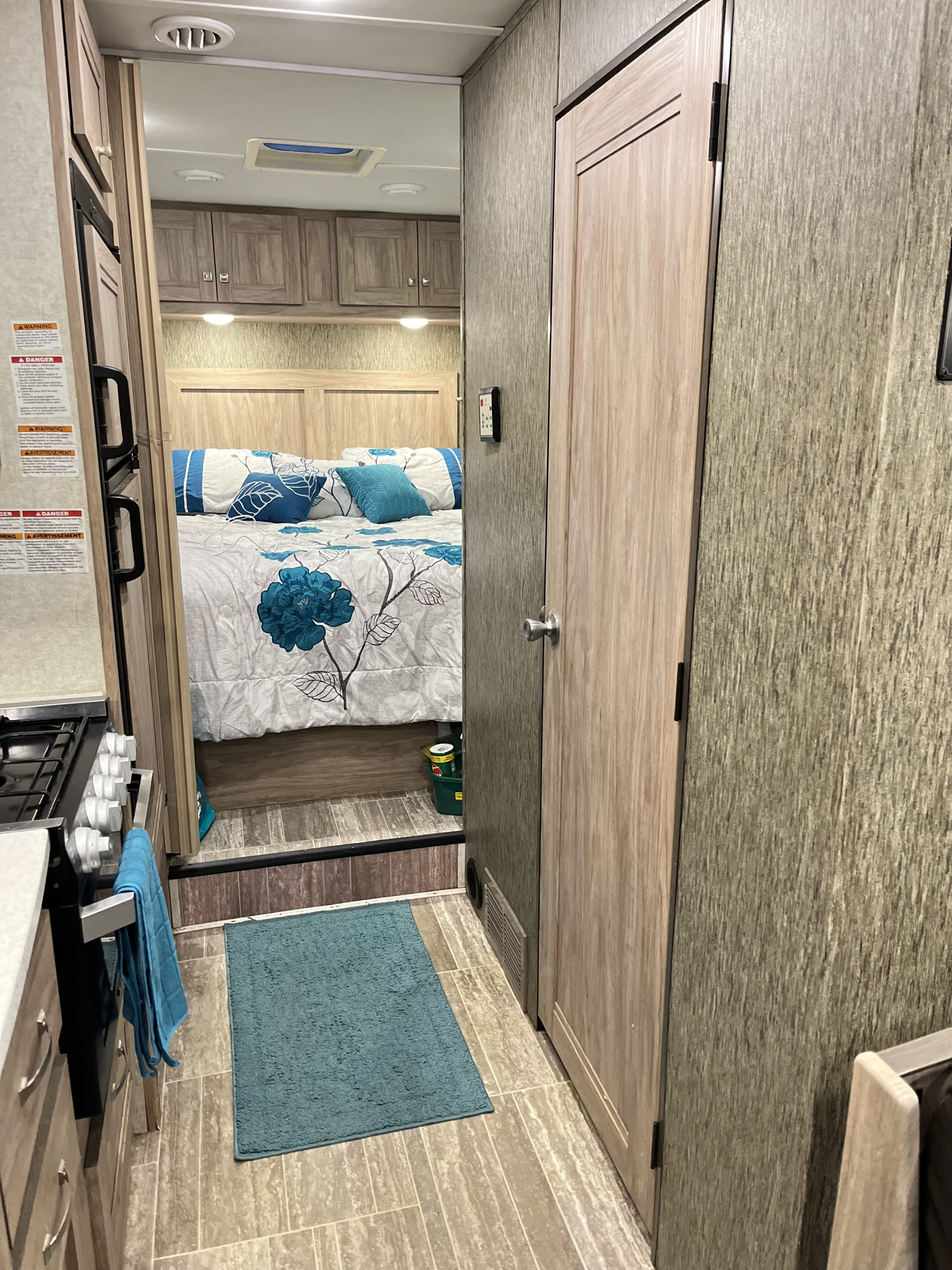 RV rental interior: kitchen galley to the left, a side door, and the bedroom with floral bedding visible ahead. Compact design.. Forest River Sunseeker 2019