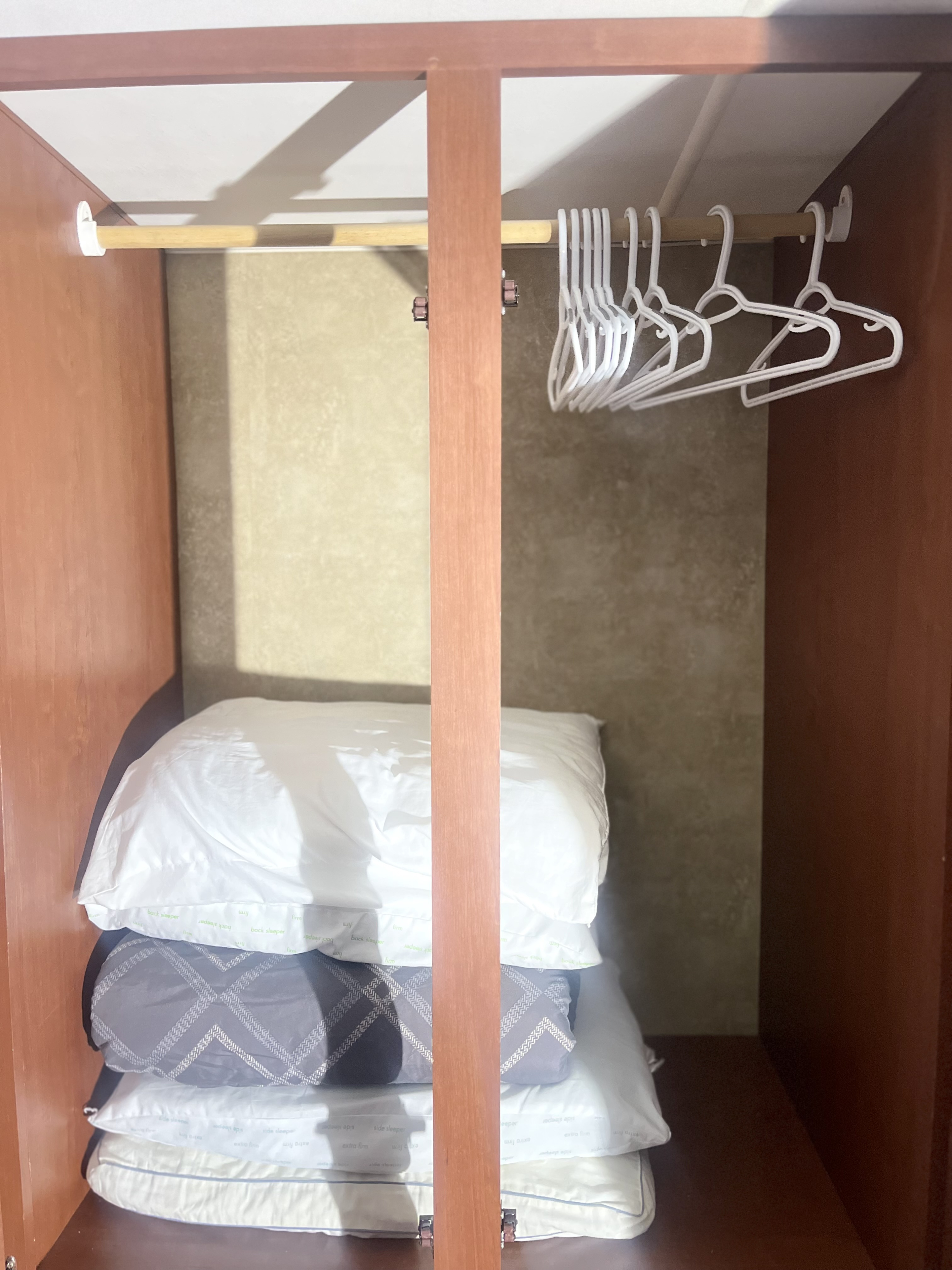 RV rental closet: a hanging rod with hangers above stacked "back sleeper" and "extra firm" pillows for travel.. Winnebago Minnie Winnie 2015