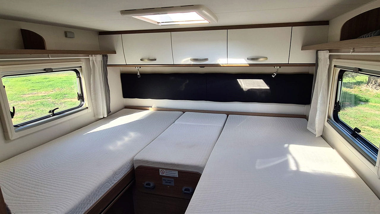 Inside a spacious RV rental: multiple comfortable beds, overhead storage, and bright windows offering scenic views.. Carado T338 2022