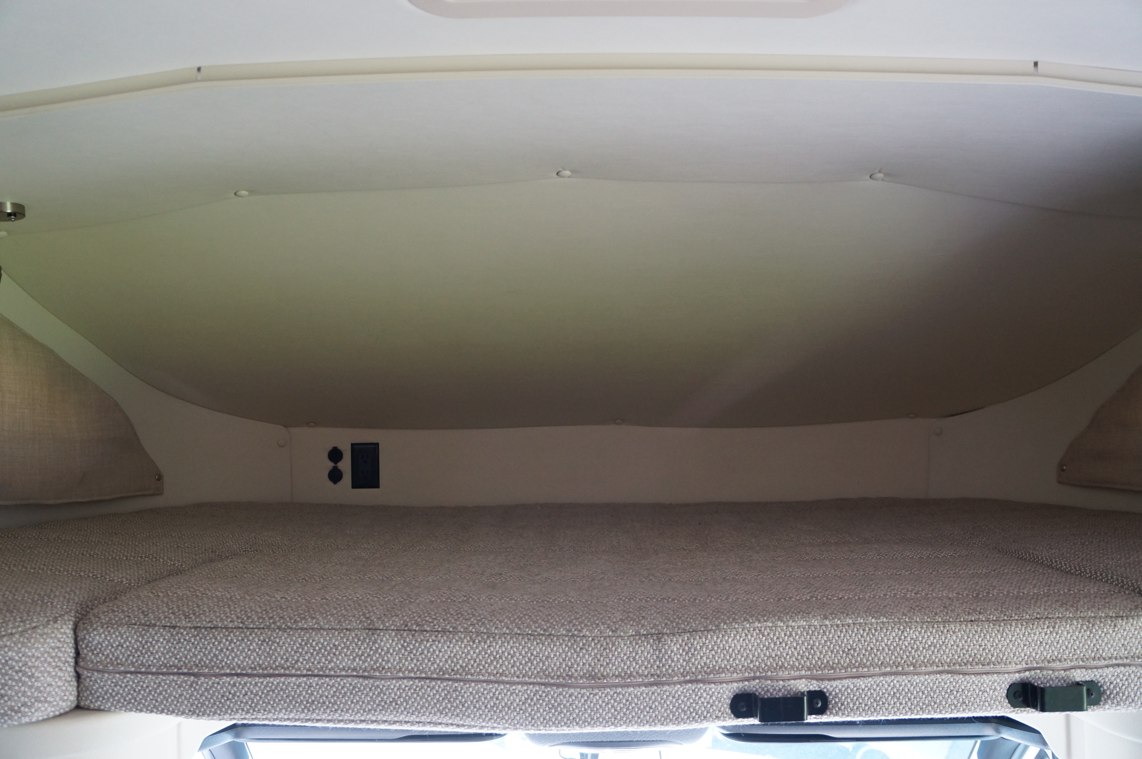 Inside an RV rental: a light-colored, upholstered overcab bunk with outlets, ready for a comfortable night's sleep.. Winnebago View 2021
