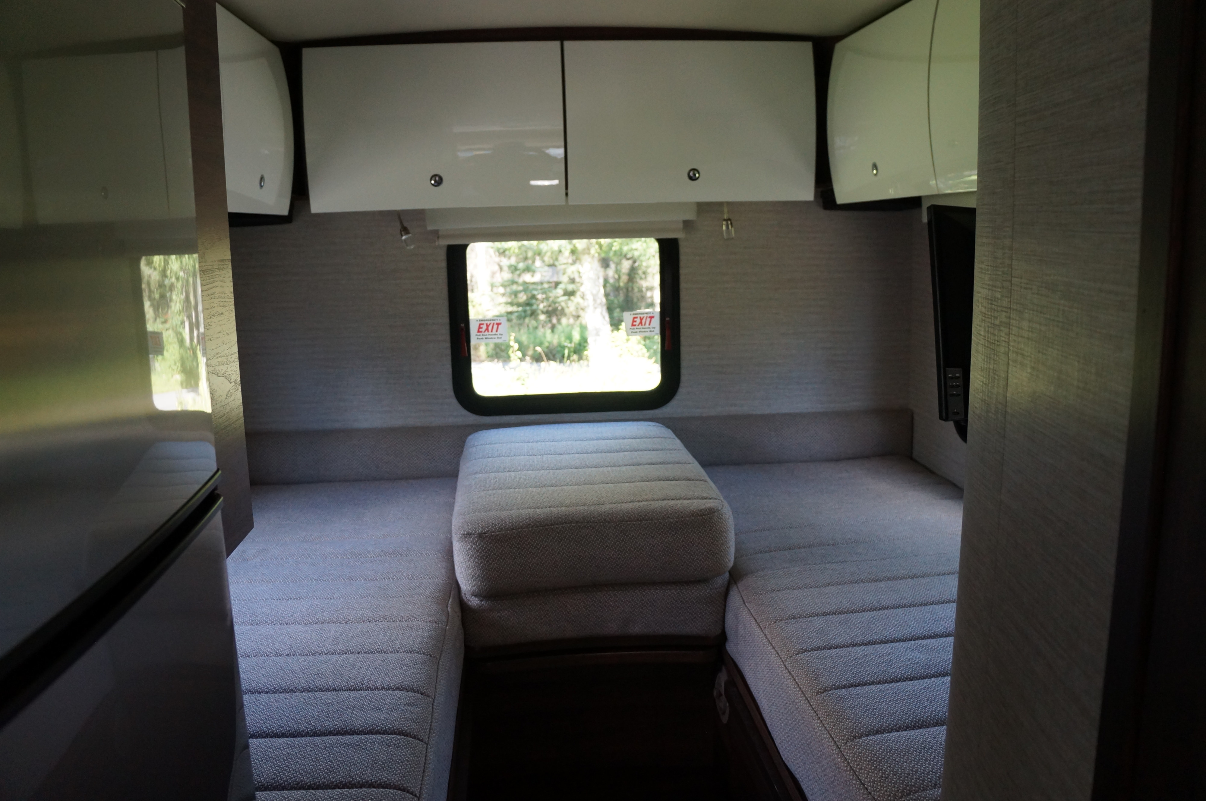 RV rental interior showing convertible bed, overhead storage, and rear window with EXIT signs.. Winnebago View 2021