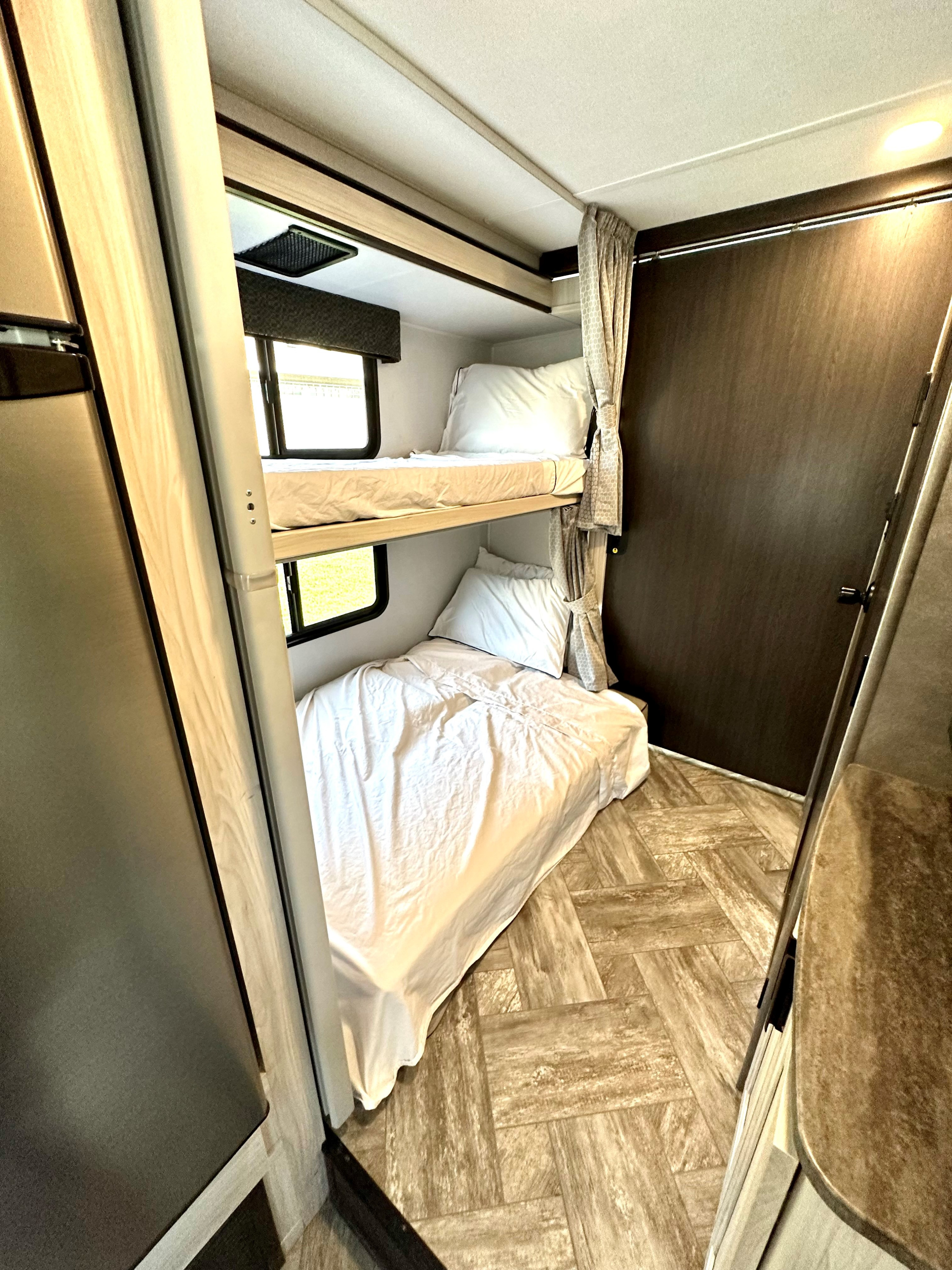 Inside an RV rental: Compact sleeping area with two bunk beds, bright windows, and tied-back curtains, providing a functional space.. Forest River Sunseeker LE 2021