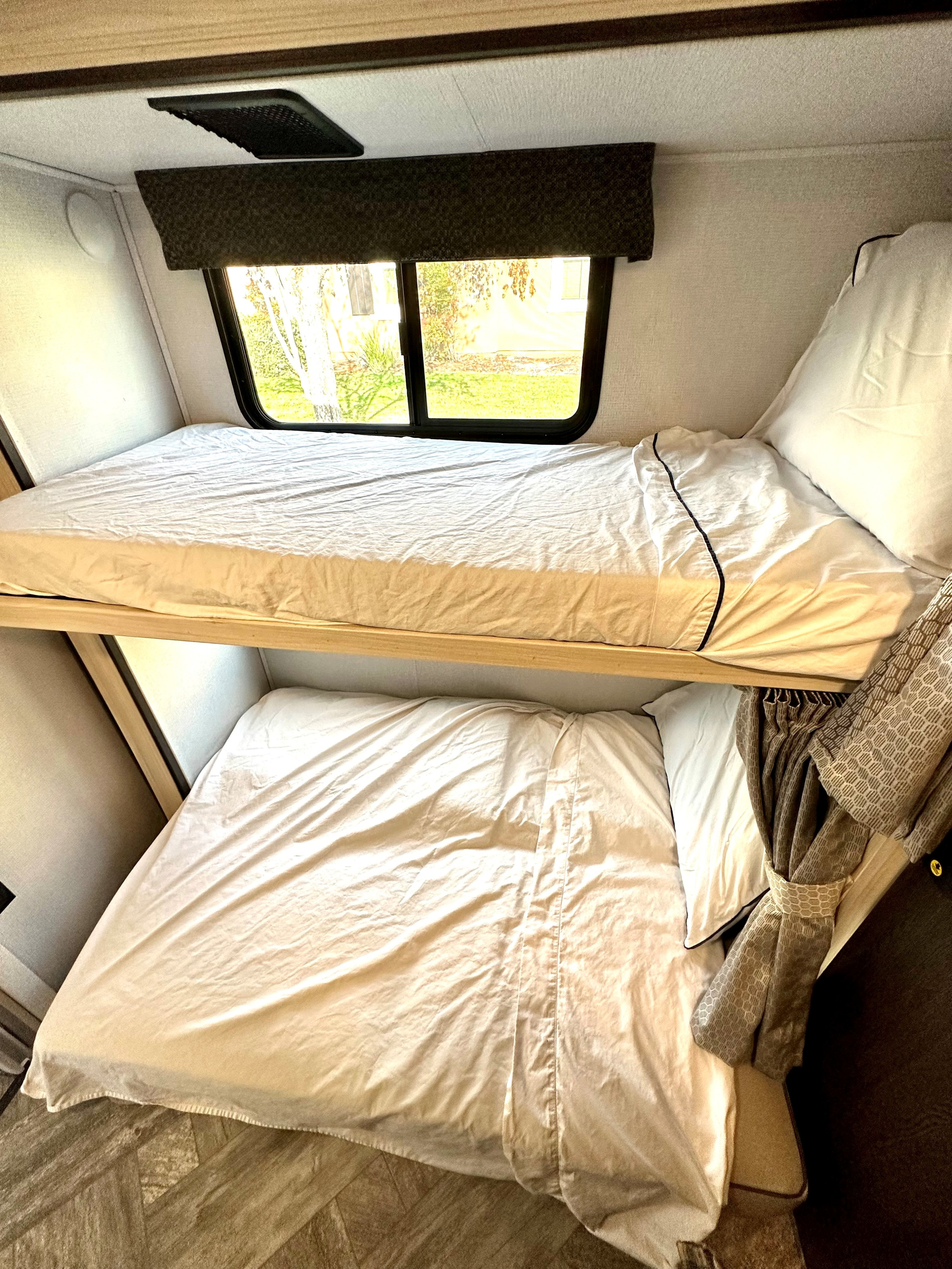 Cozy bunk beds in an RV rental, featuring white sheets, a window view from the top bunk, and a patterned curtain.. Forest River Sunseeker LE 2021