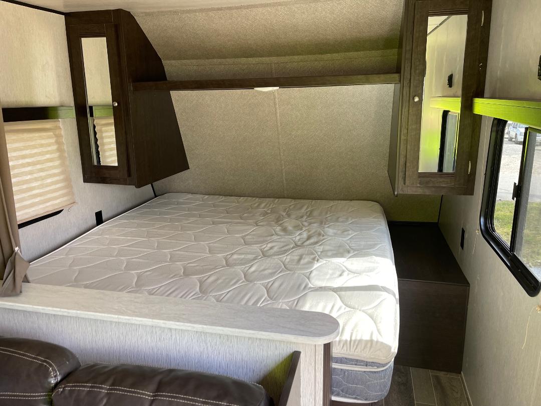 RV rental interior: a bedroom with a bed, mirrored overhead storage, and a window with blinds. Ready for adventure.. Heartland RVs Trail Runner SLE 2019