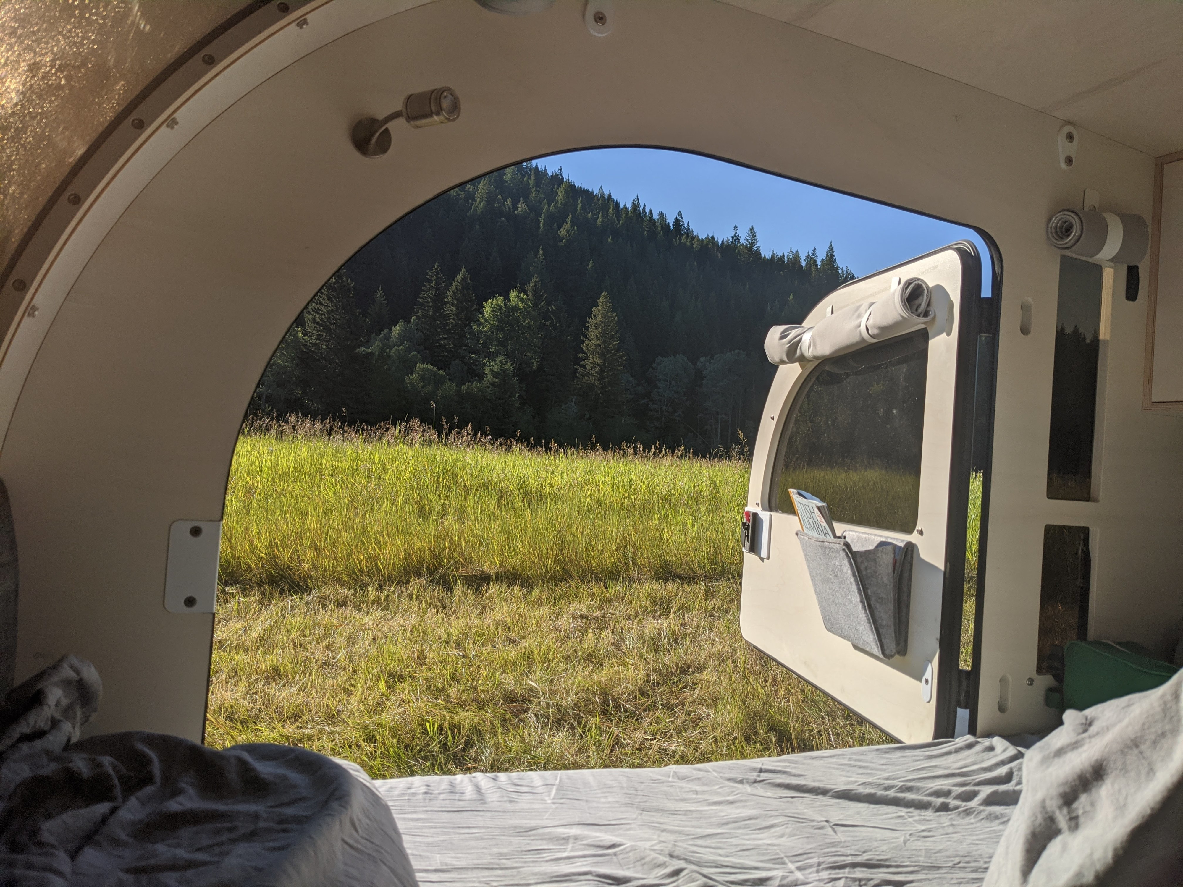 Enjoy a serene nature view from this cozy RV rental bed, overlooking a vibrant green field and dense forest.. droplet XL 2023