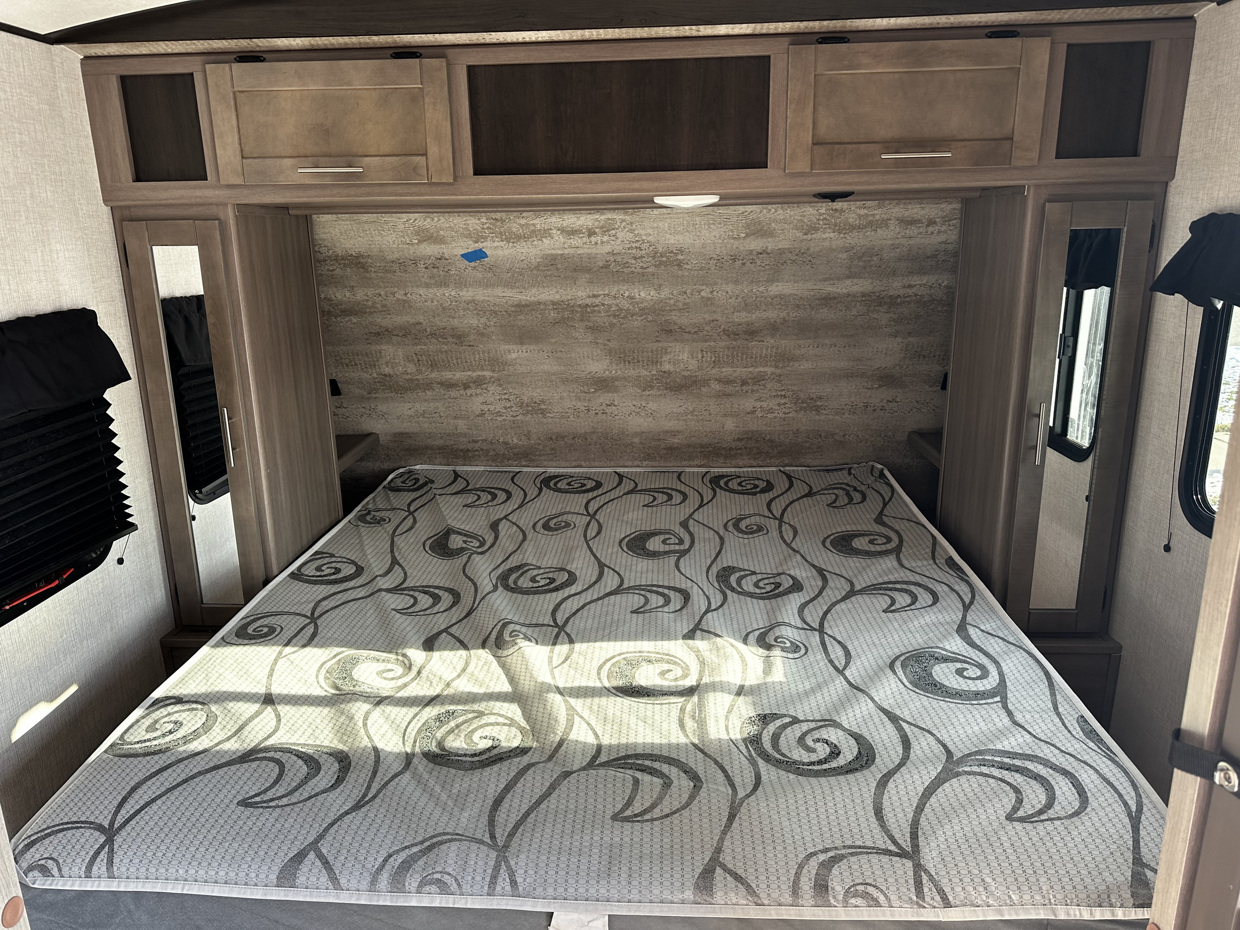 This RV rental's cozy bedroom offers a patterned bed, wood cabinets, and mirrored wardrobes, illuminated by sunlight.. Crossroads RV Sunset Trail Super Lite 2021