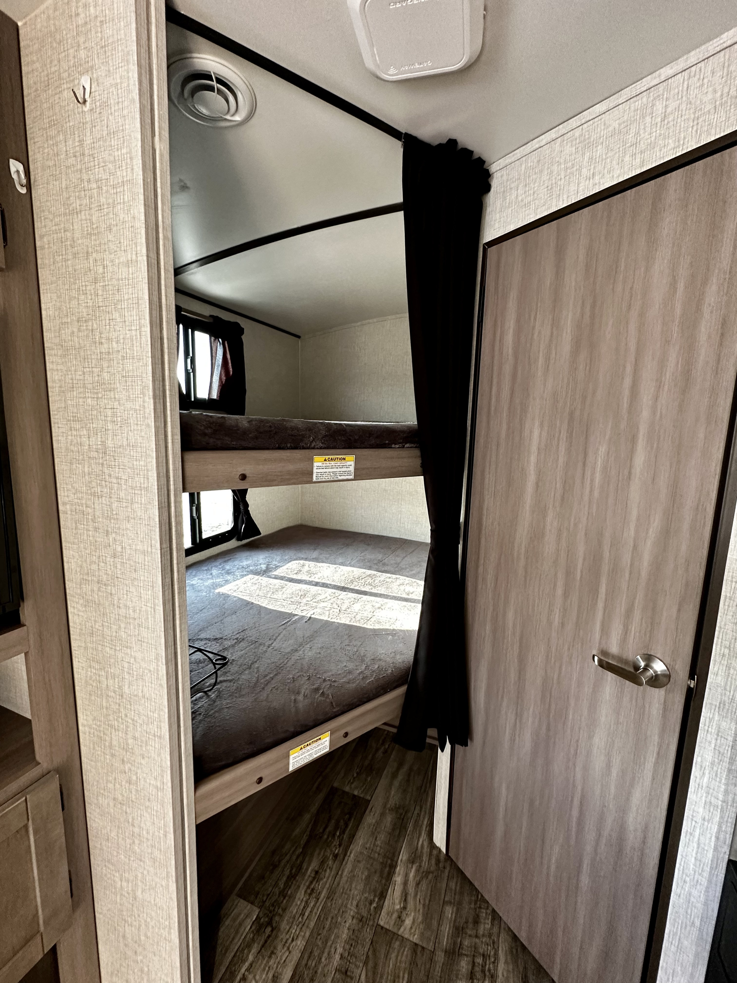 This RV rental features compact bunk beds with privacy curtains, light wood finishes, and a window, ideal for extra sleeping.. Crossroads RV Sunset Trail Super Lite 2021