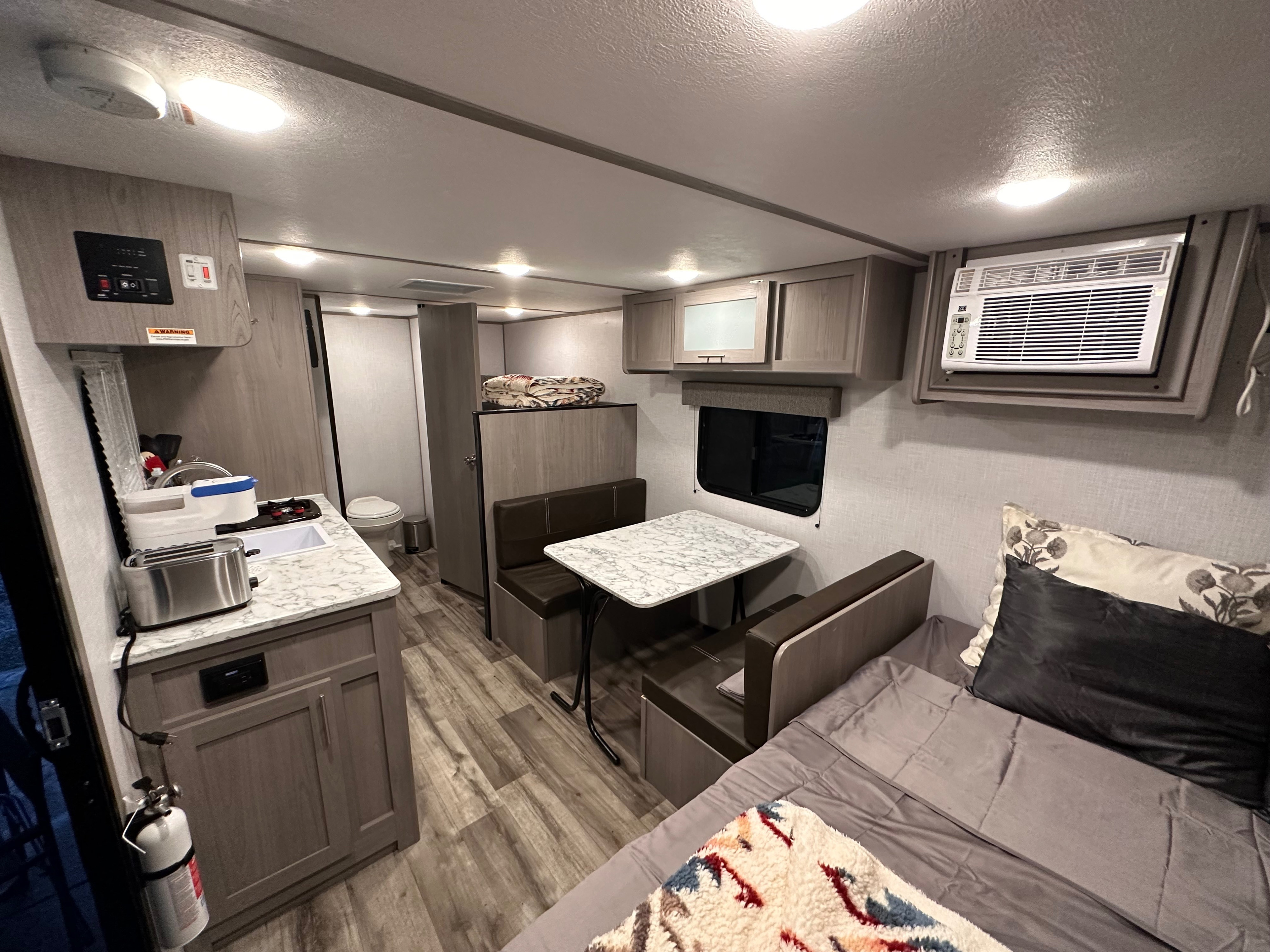 This RV rental offers a compact, functional interior: a well-lit kitchen counter, dining booth, and sleeping area with a bed.. Coleman LANTERN LT 17B 2023