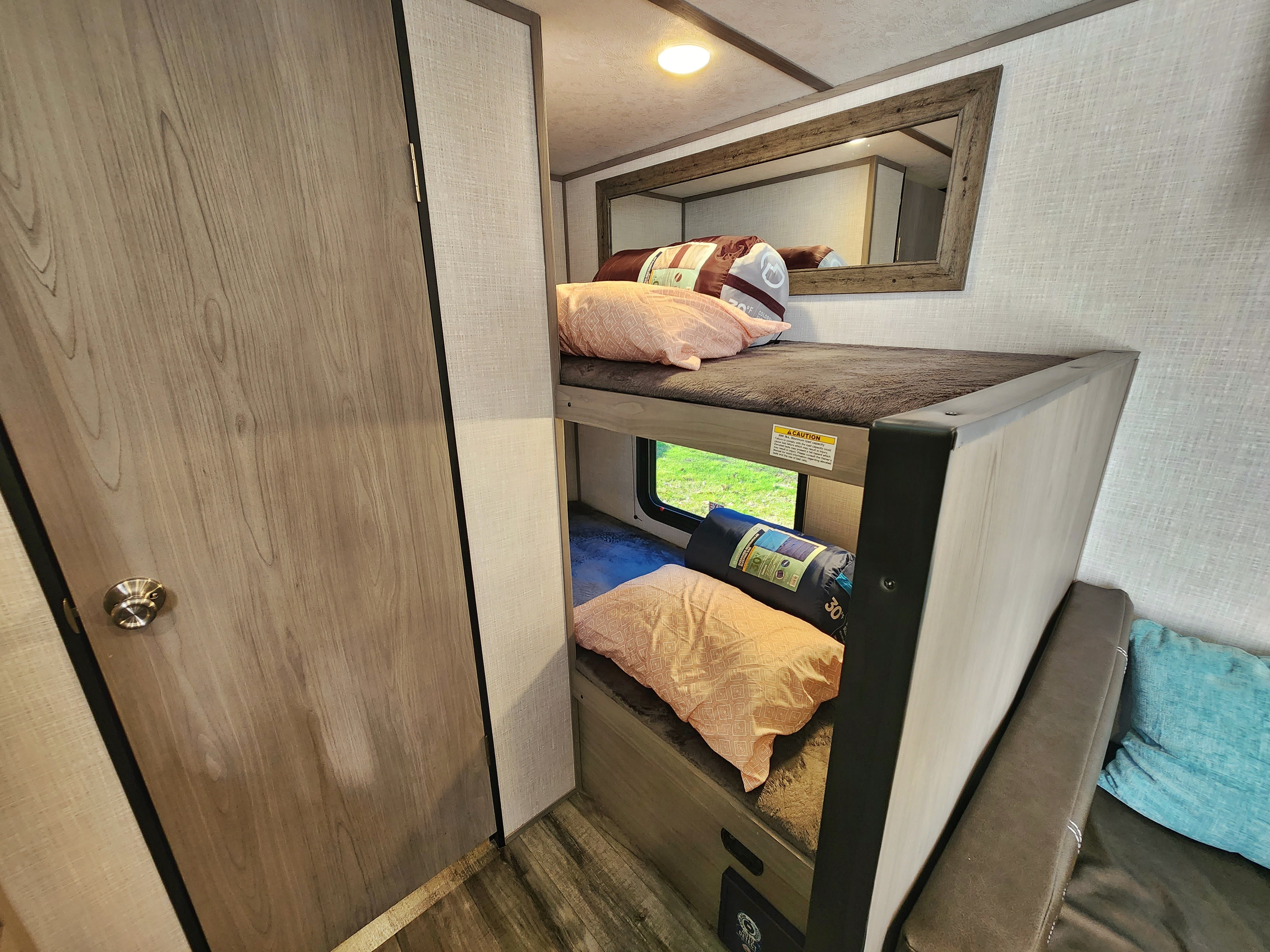 Cozy RV rental interior featuring comfortable bunk beds with pillows, sleeping bags, and a window view. Ideal for family trips.. Coleman Lantern 2023