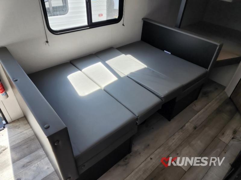 Inside an RV rental: Grey cushions form a dinette that converts to a bed, brightened by sunlight.. Keystone Springdale 2022