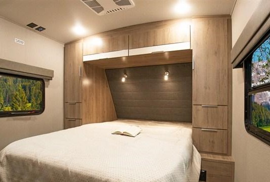 This RV rental's cozy bedroom features a bed, wooden cabinets, and a scenic window view. Ideal for comfortable travel.. Grand Design Imagine 2021