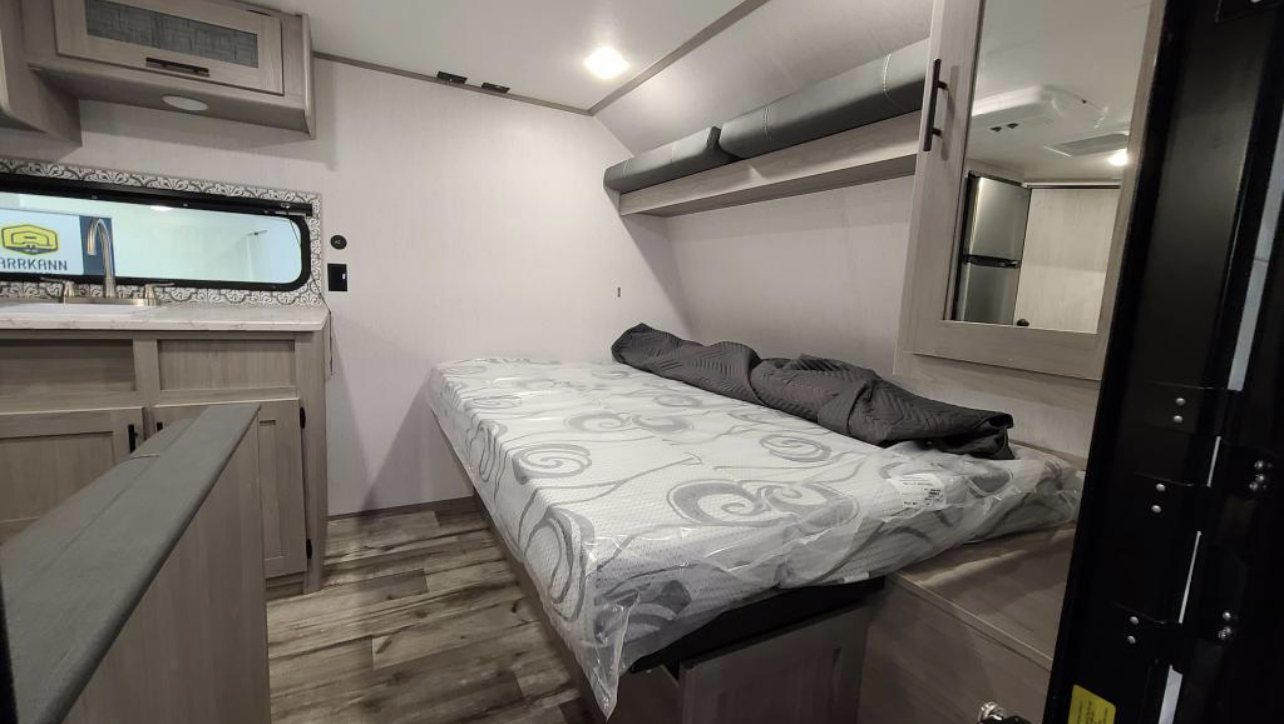 RV rental interior: a compact bed with storage, an overhead bunk, and a small kitchen counter with sink. Practical living space.. Dutchmen Coleman Lantern LT 2021