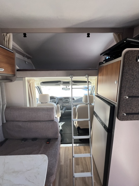 Inside an RV rental: a ladder leads to an overhead bunk. Living area, driver's cabin, and fridge visible. Ready for adventures!. Rimor SEAL 5 (II) 2025