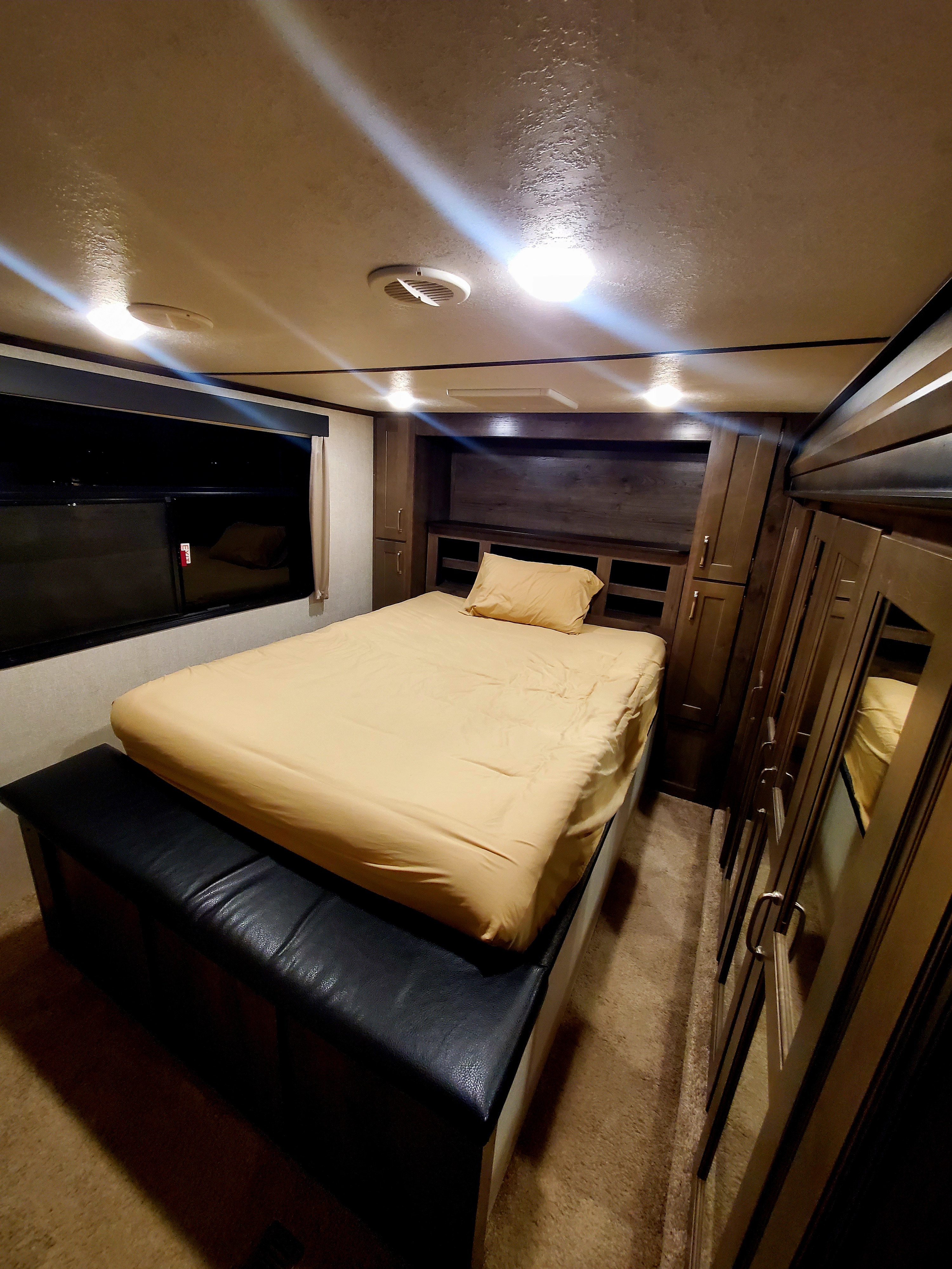 Comfortable RV rental bedroom with warm lighting, featuring a spacious bed, built-in storage, and mirrored wardrobe.. Keystone RV Montana High Country Toy Hauler 2019