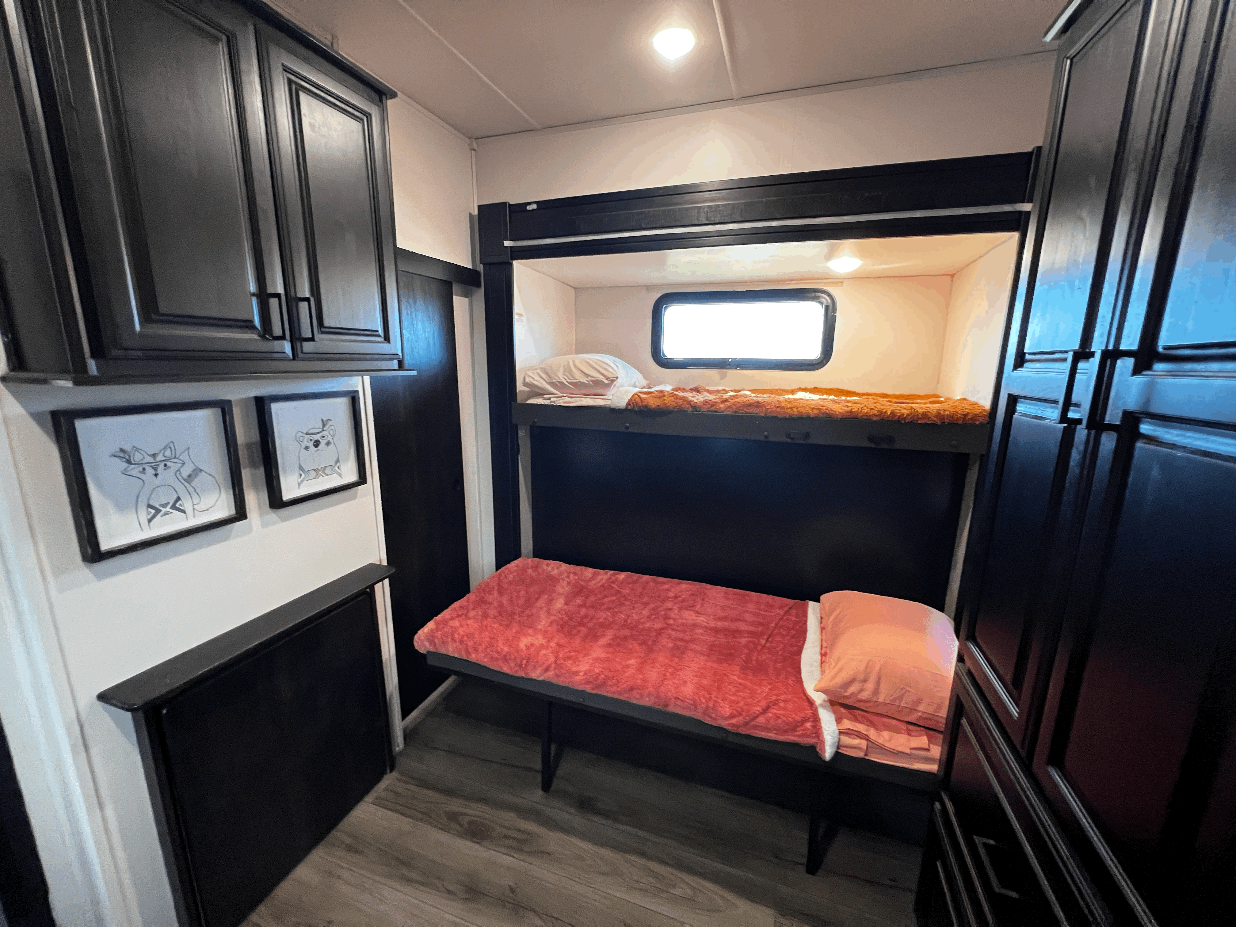Inside this RV rental, find cozy black bunk beds with a window on the top bunk, plus dark cabinets and animal artwork.. Highland Ridge RV Silverstar 2021