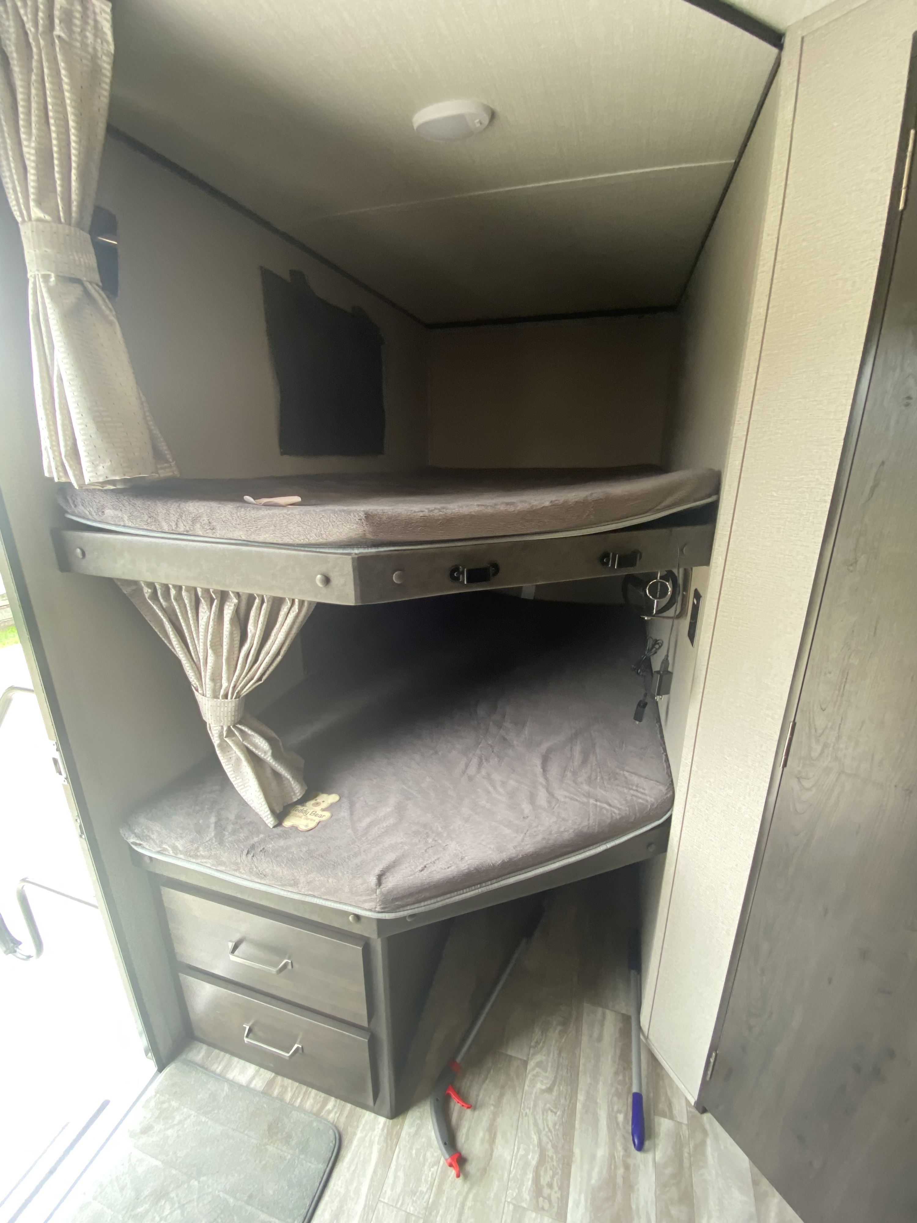 Cozy RV rental bunk beds with privacy curtains, storage drawers, and essential cleaning tools below.. Grand Design Transcend 2020