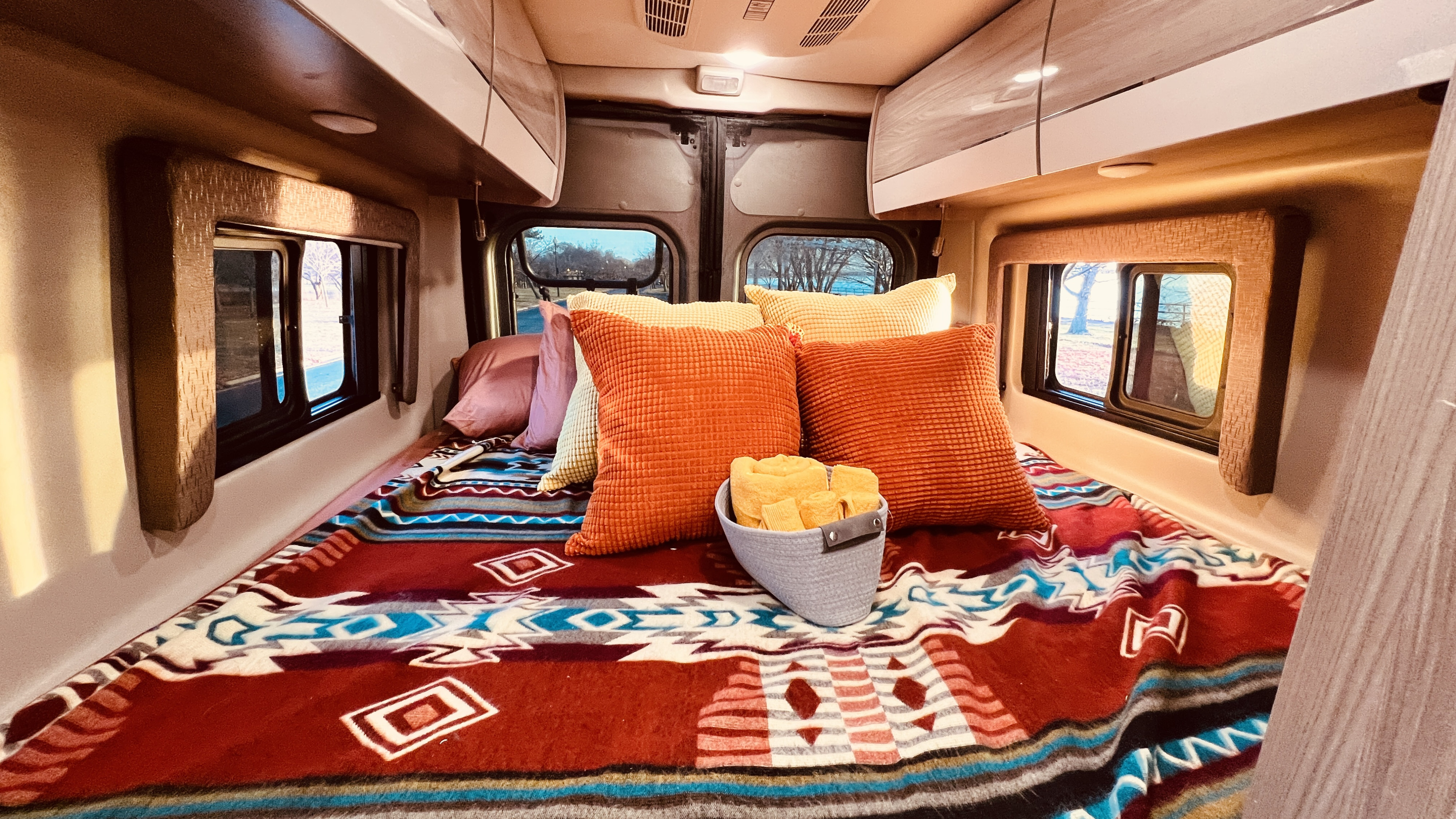 Cozy RV rental bed with a colorful Southwestern-style blanket, plush pillows, and a view outside for your adventure.. Thor Sequence 2022