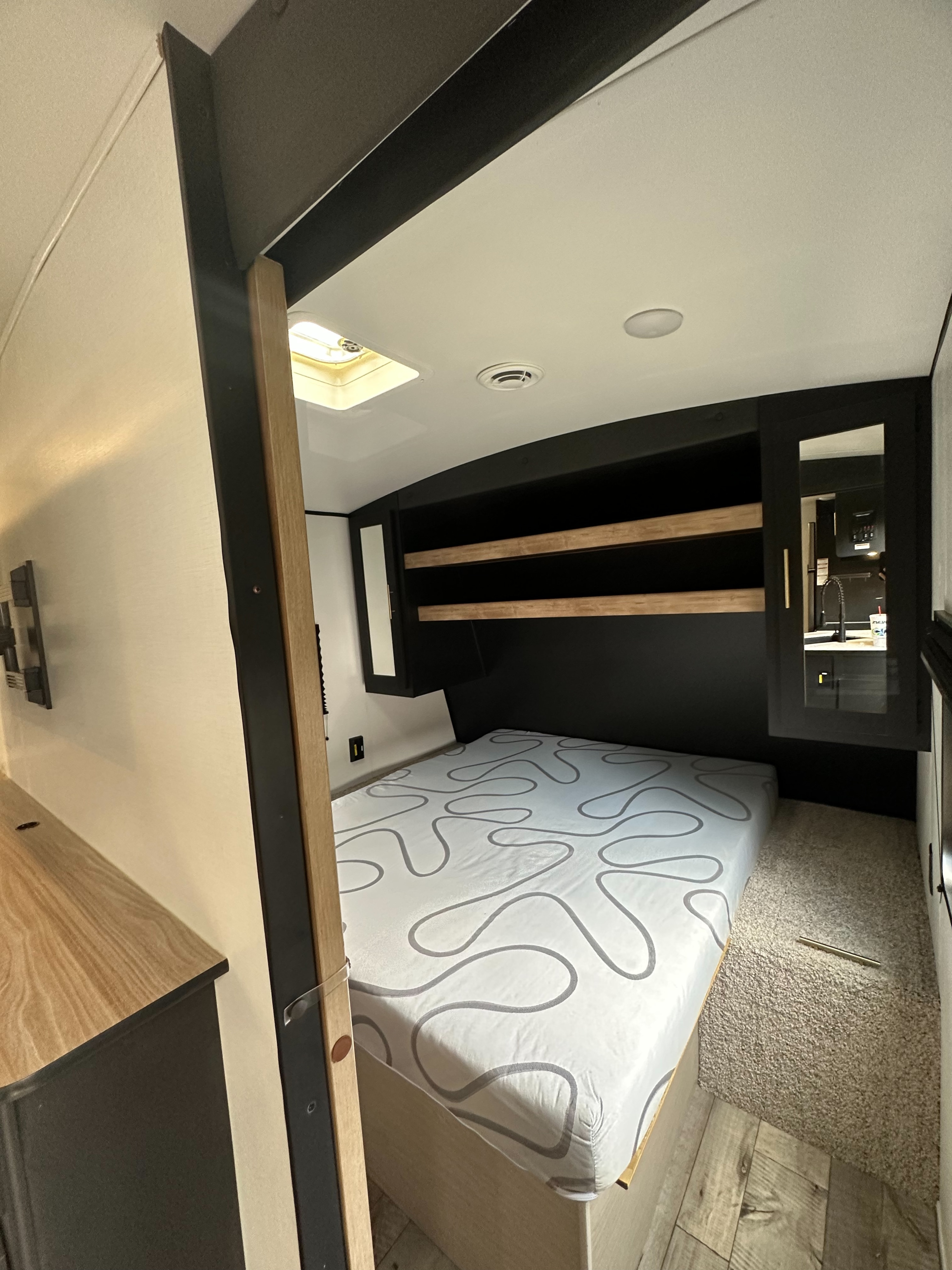 Inside a stylish RV rental: a cozy bedroom features storage and an adjoining kitchen view from the mirrored cabinet.. Keystone RV Springdale 2022