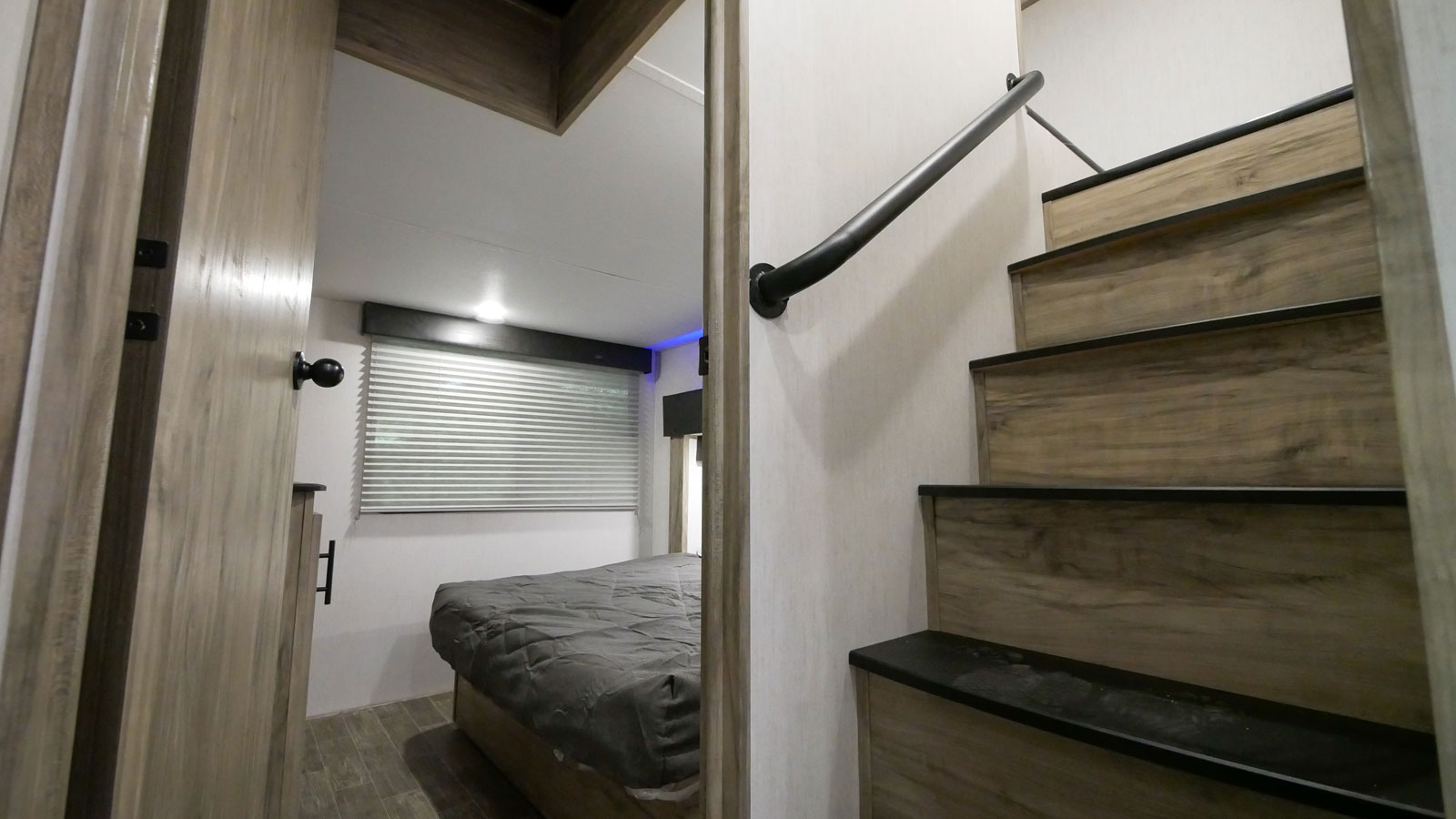 Modern RV rental interior with a cozy bedroom visible through an open door, beside a sleek staircase featuring a black handrail.. Forest River Cherokee Arctic Wolf 2022