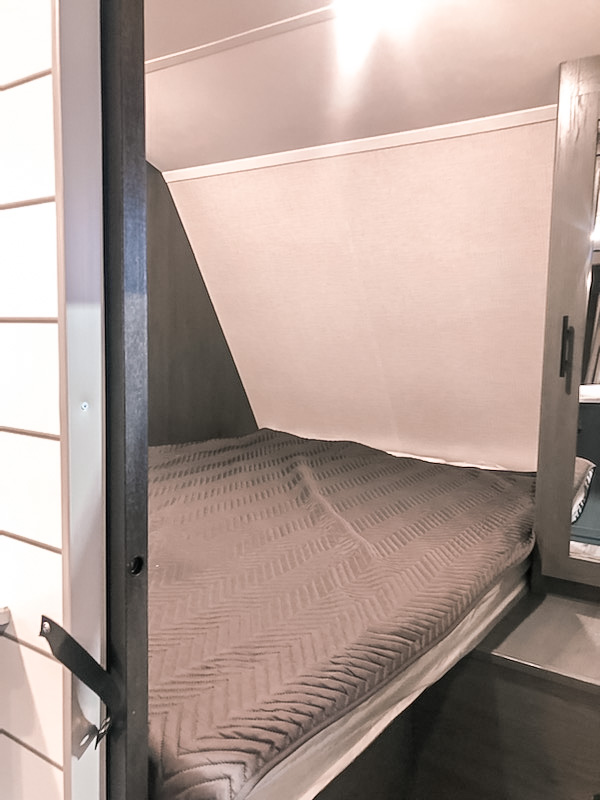 Inside an RV rental: a cozy bunk bed with a quilted grey cover. Perfect for road trip sleep.. Dutchmen Colorado 2022