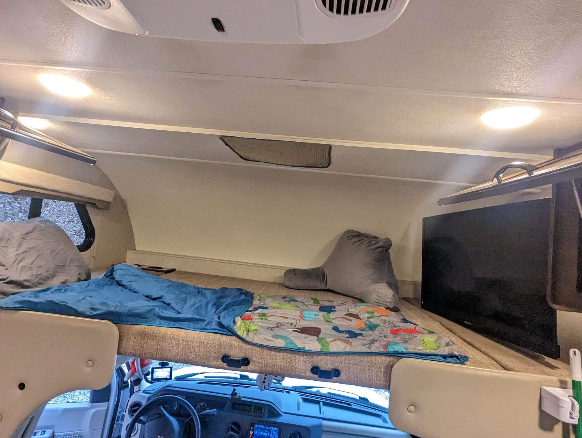 RV rental over-cab bunk bed with cozy bedding, reading pillow, and TV. Perfect setup for family comfort on the road.. Thor Freedom Elite 2020