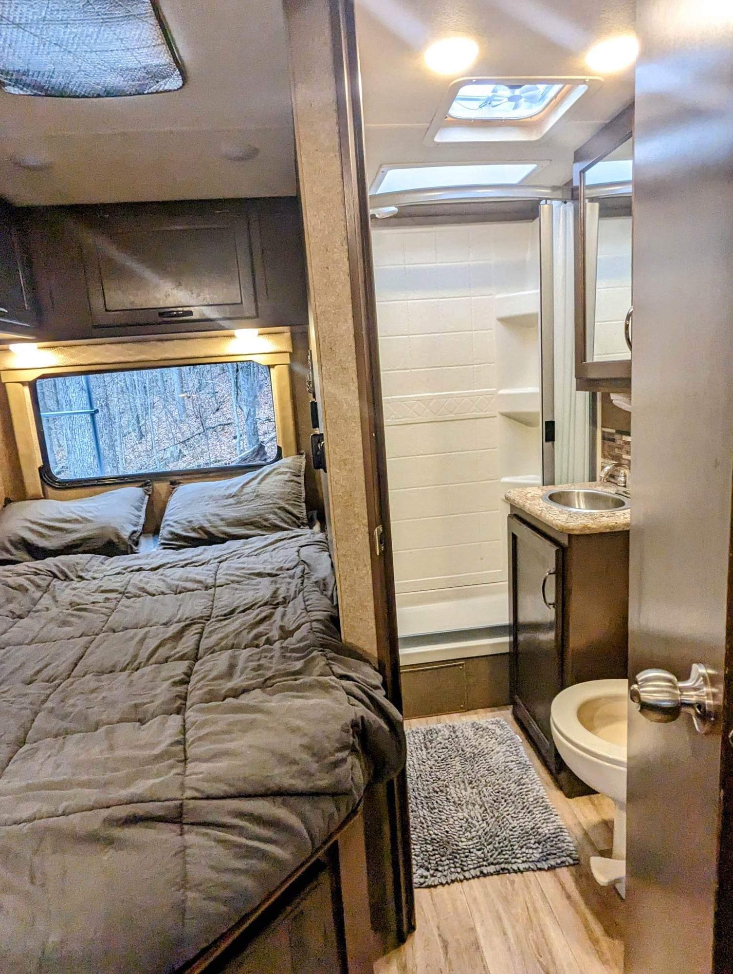 Cozy rv rental interior with a comfortable bed, window views, and a compact bathroom featuring a shower, sink, and toilet.. Thor Freedom Elite 2020