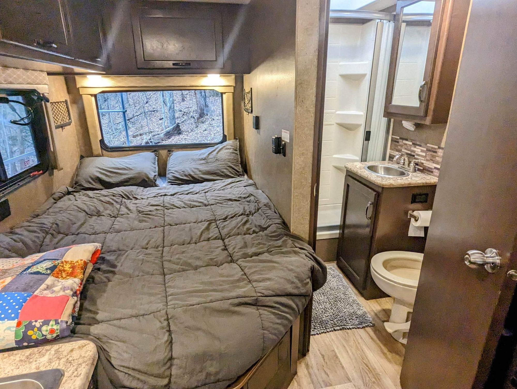 This RV rental showcases a cozy bedroom with a large bed, windows, and an adjacent compact bathroom with a shower, sink, and toilet.. Thor Freedom Elite 2020
