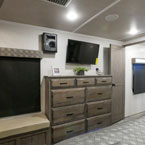 Modern RV rental bedroom features a long wooden dresser, mounted TV, and an entertainment unit on the wall.. Cedar Creek Champagne 2021