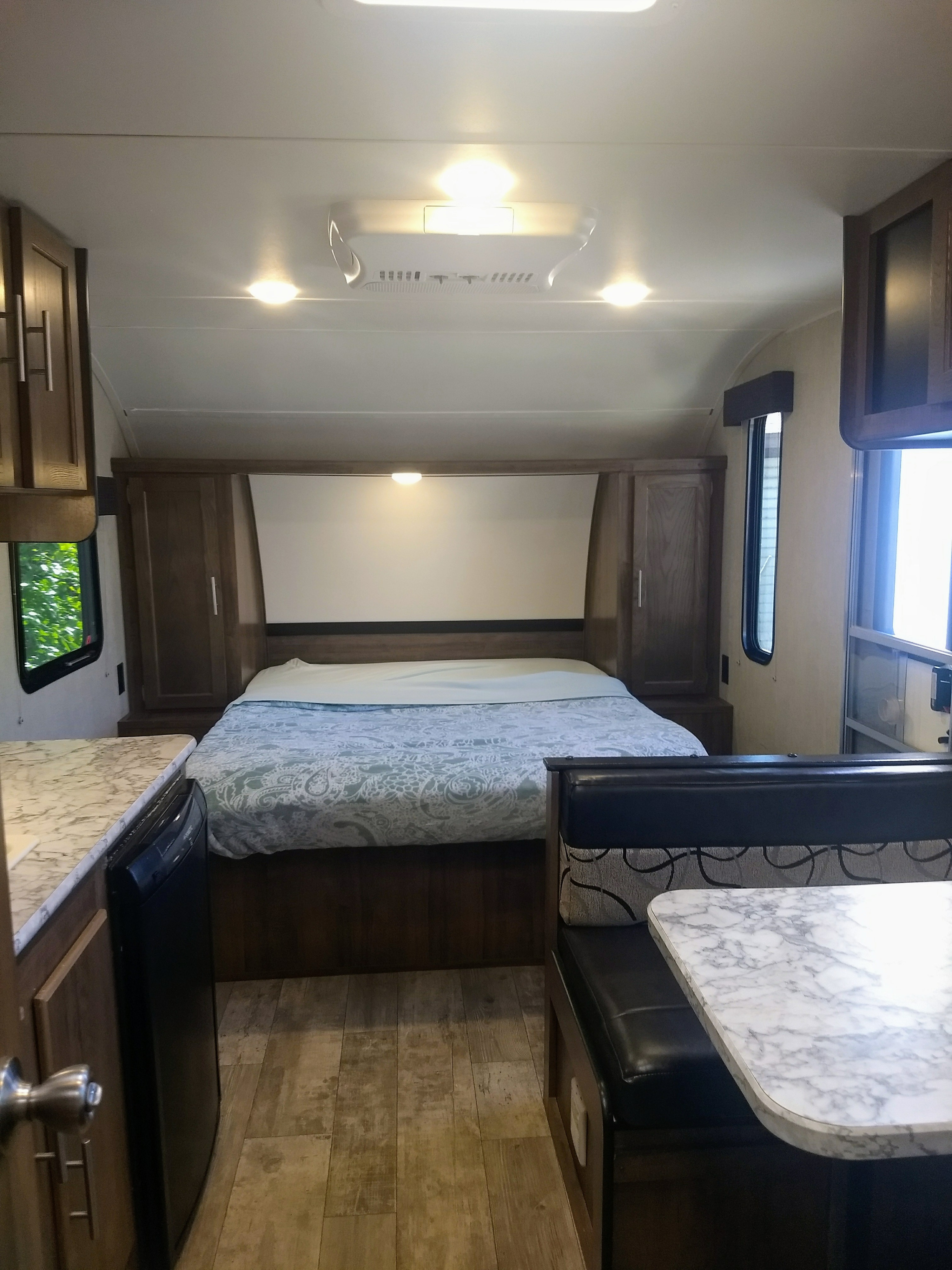 Inside this RV rental: a well-appointed bedroom with bed, compact kitchen counter, and dining booth for your travels.. Gulf Stream Amerilite 2019