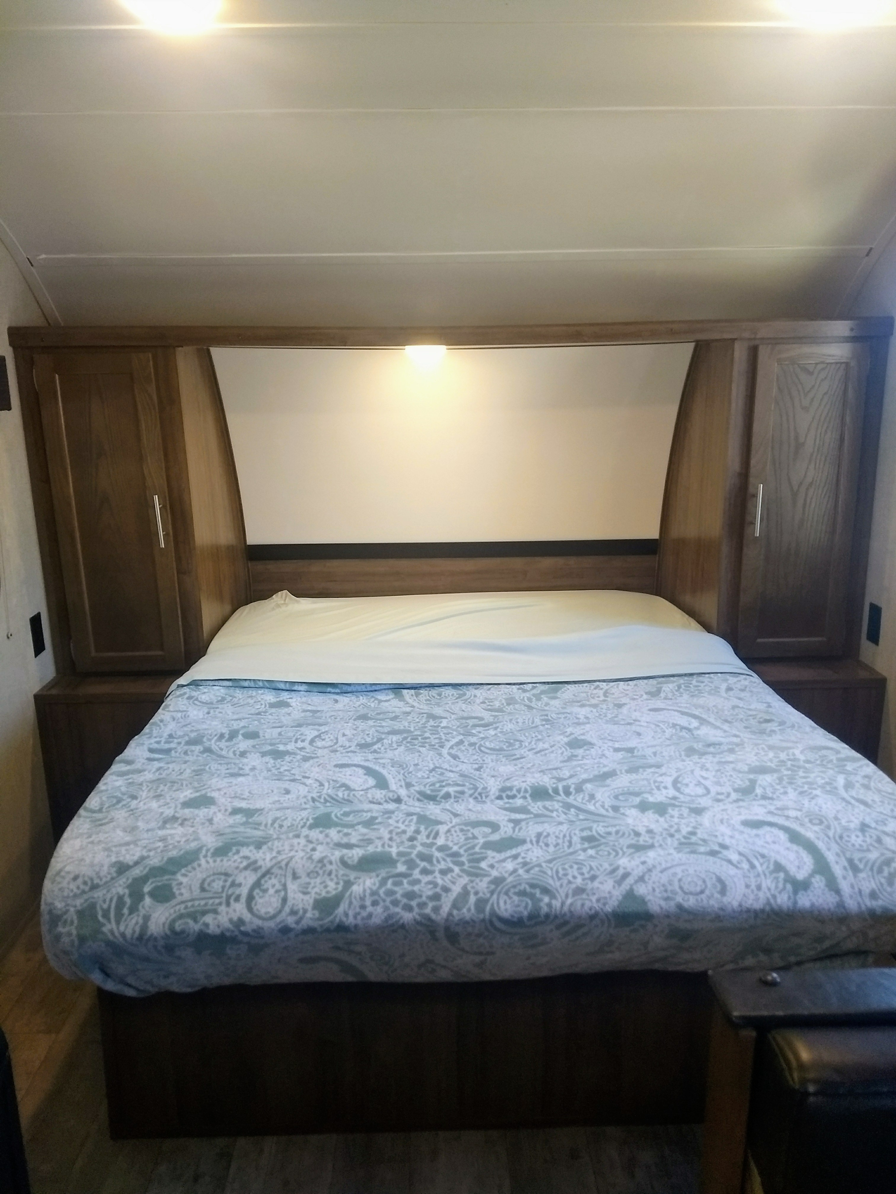 Inside an RV rental: a comfortable bedroom featuring a bed with patterned covers, built-in cabinets, and a headboard light.. Gulf Stream Amerilite 2019