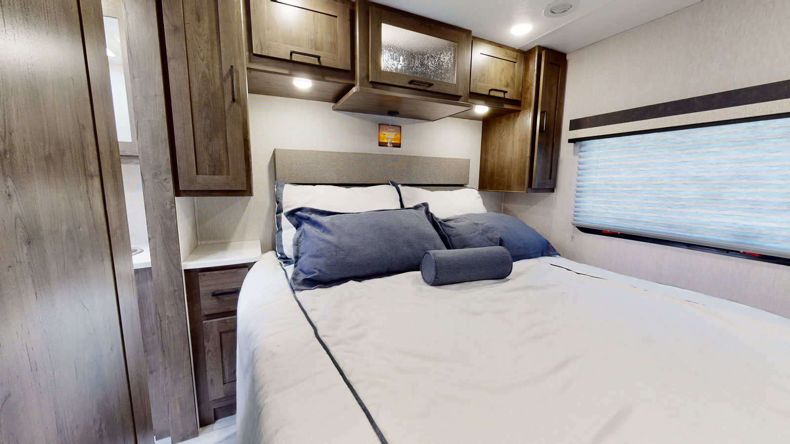 Cozy RV rental bedroom: bed with blue pillows, wood cabinetry, window blinds. Perfect for travel.. Coachmen MIRADA 35ESF 2026
