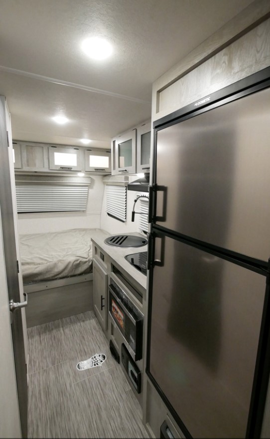 Modern RV rental interior showcasing a compact kitchen, stainless steel fridge, and cozy bed area with blinds.. Ibex 19QHT 2022