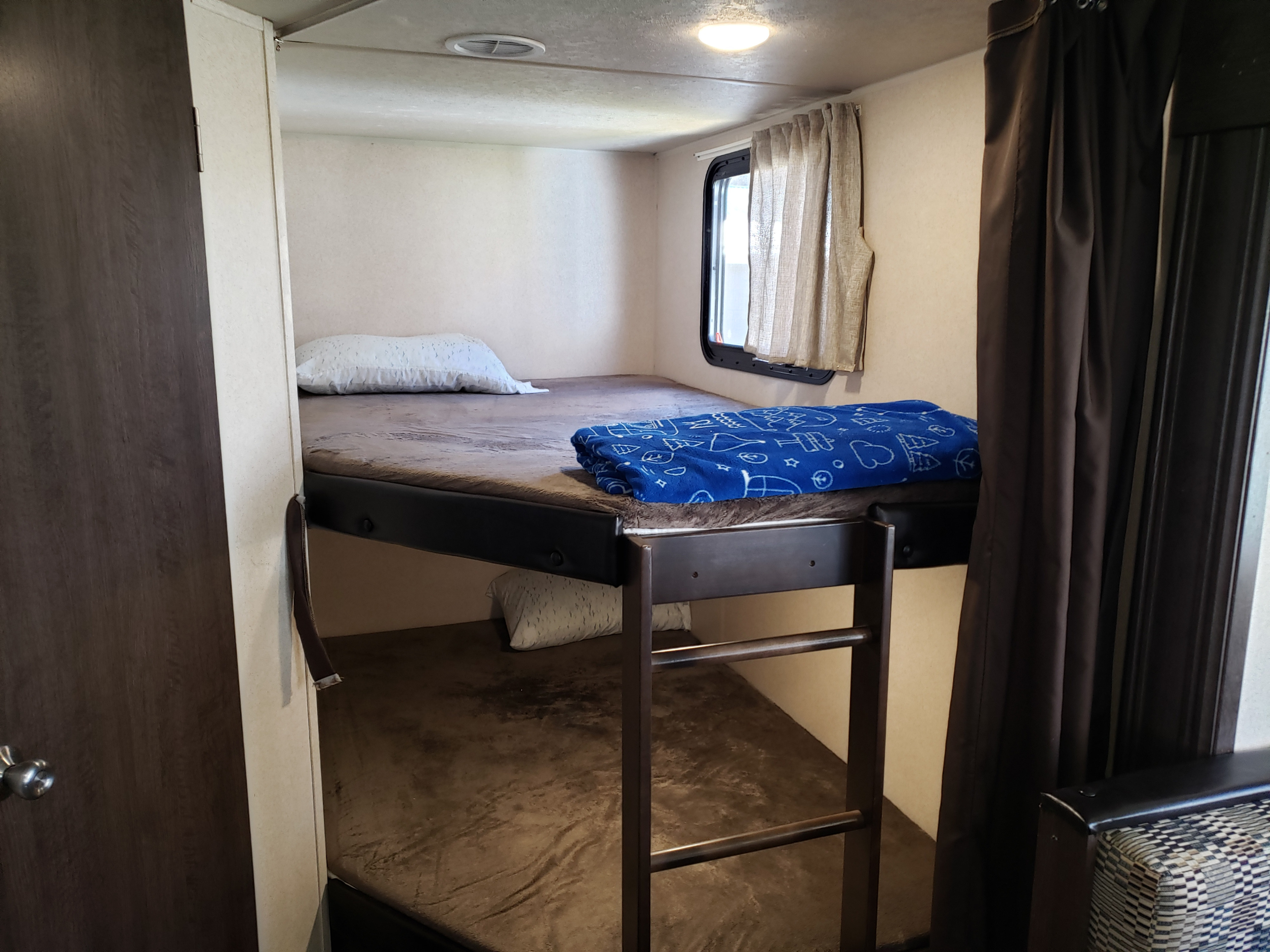 Inside an RV rental: two bunk beds with pillows and a blue blanket, providing a compact and cozy sleeping area for travelers.. Forest River Wildwood X-Lite 2018