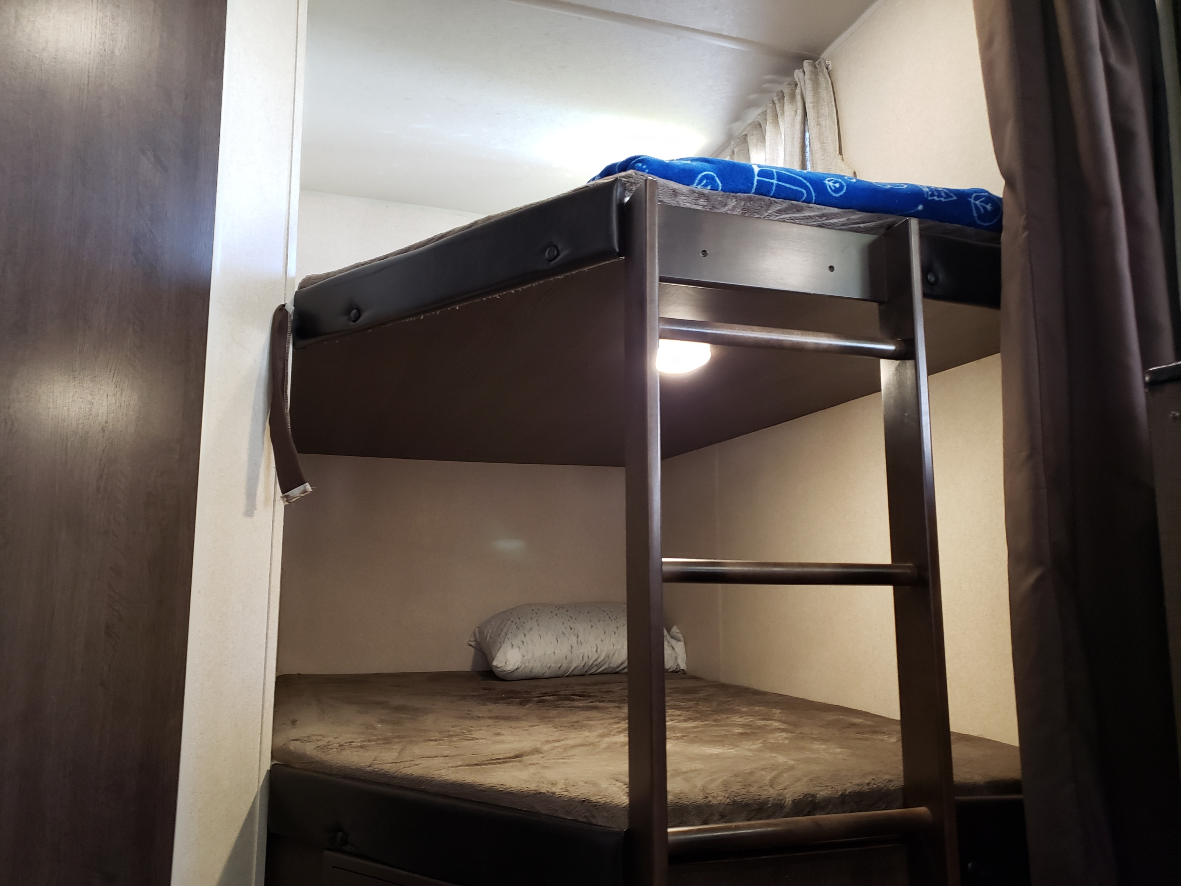 Inside an RV rental: two bunk beds, a ladder to the top, a reading light, and privacy curtains for a cozy sleep.. Forest River Wildwood X-Lite 2018