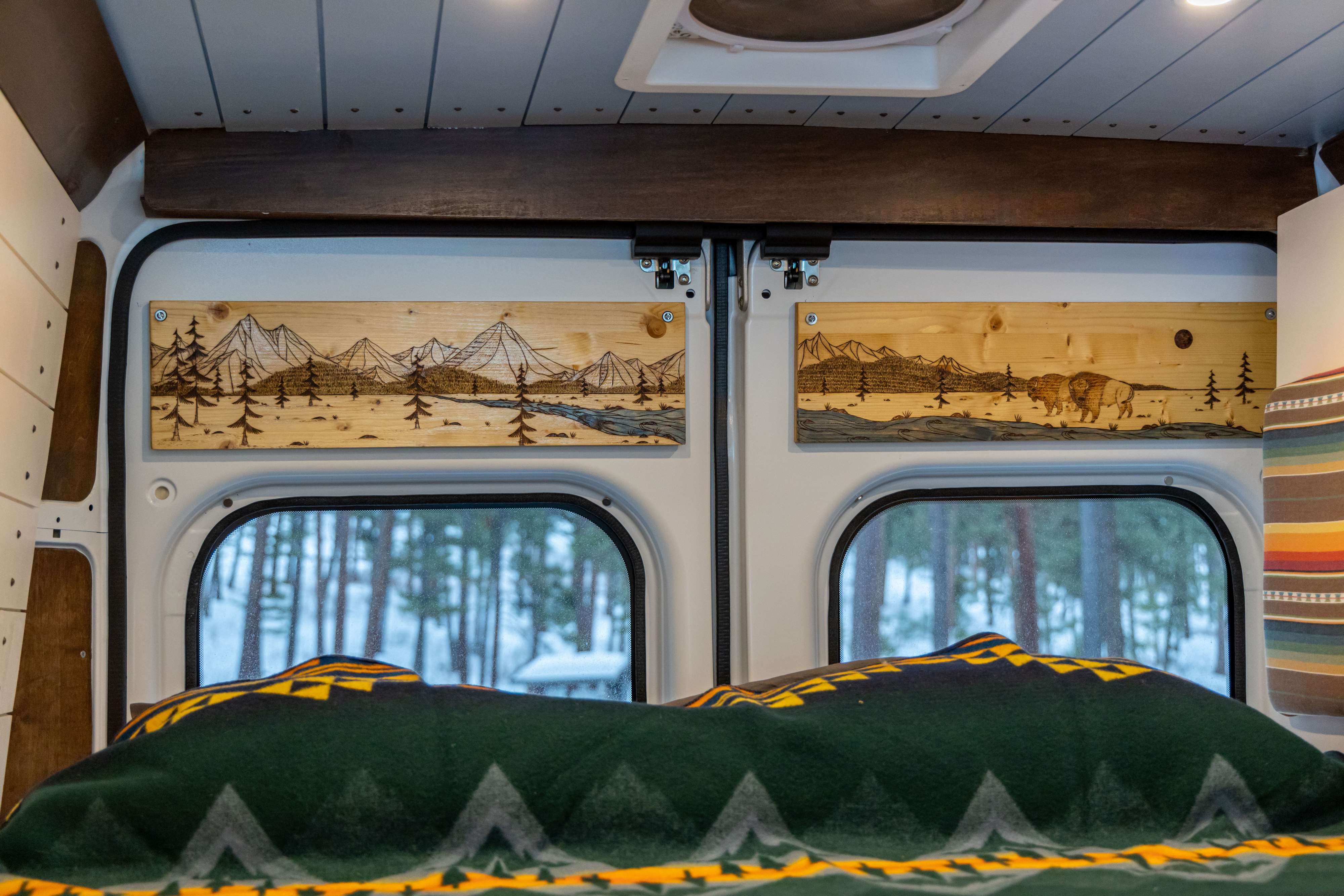 Cozy RV rental interior with custom wood art of mountains & bison, offering snowy forest views from the bed.. Dodge Ram Promaster 2500 2020