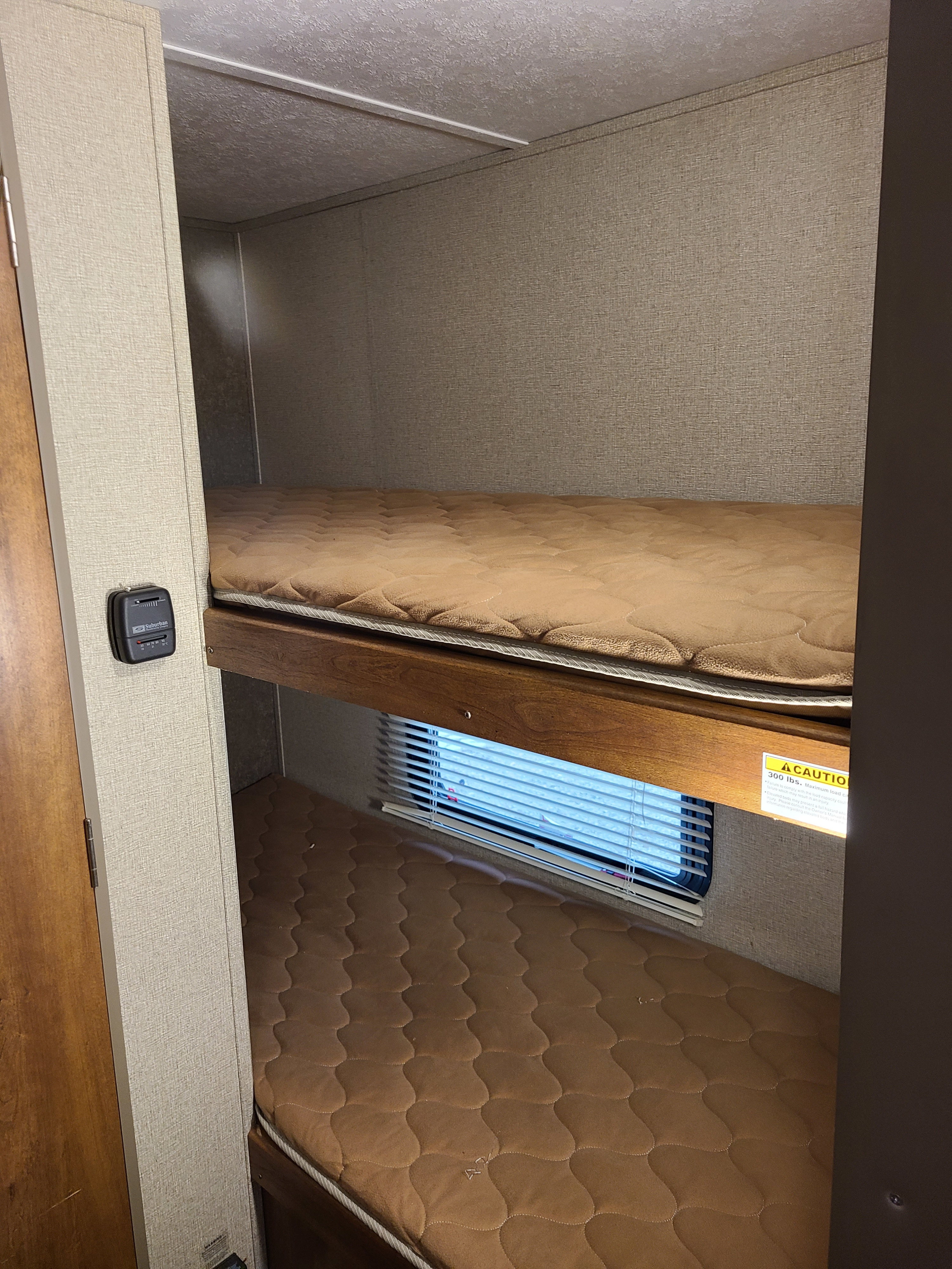 RV rental bunk beds with brown mattresses. Top bunk notes a 300 lbs max load. Also visible: window and thermostat.. Keystone RV Summerland Mini 2017