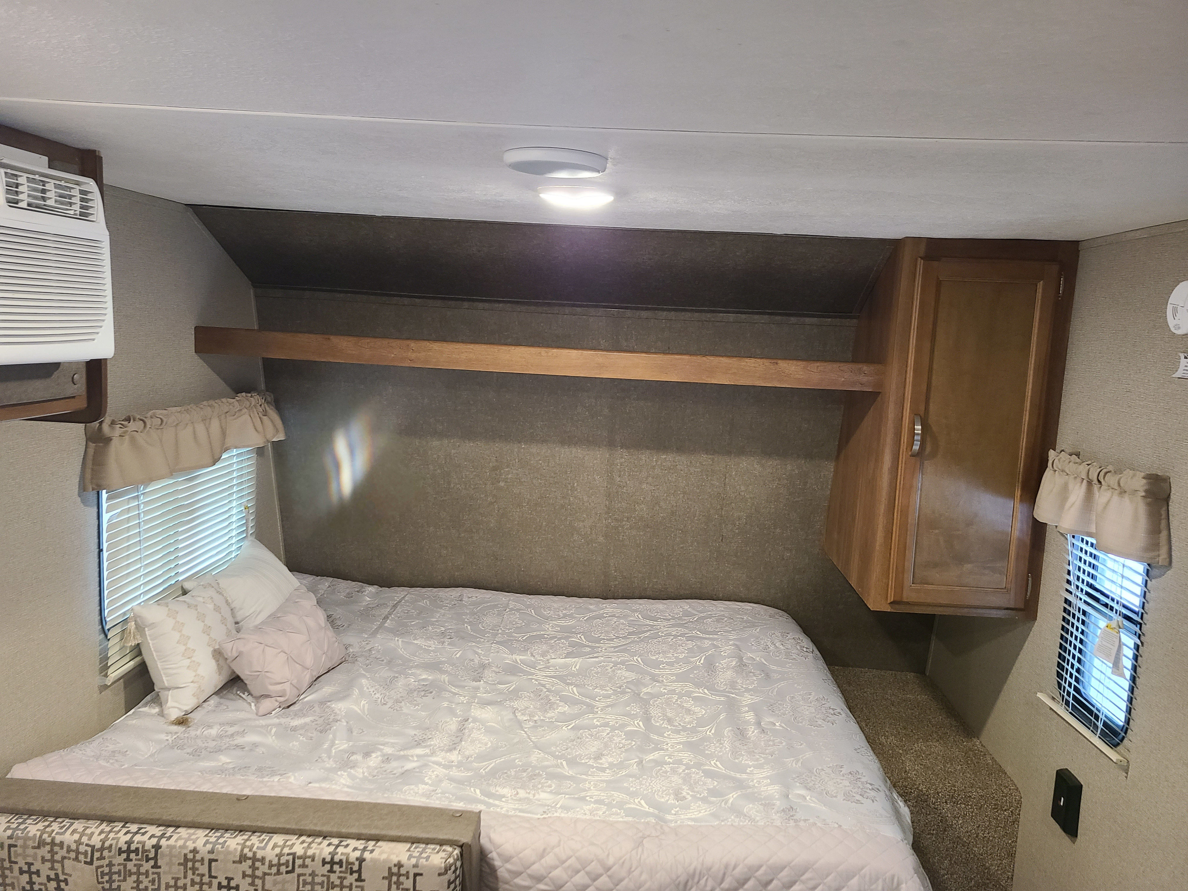 Cozy RV rental bedroom with a comfy bed, AC unit, window, and storage cabinets. Ideal for travel accommodations.. Keystone RV Summerland Mini 2017