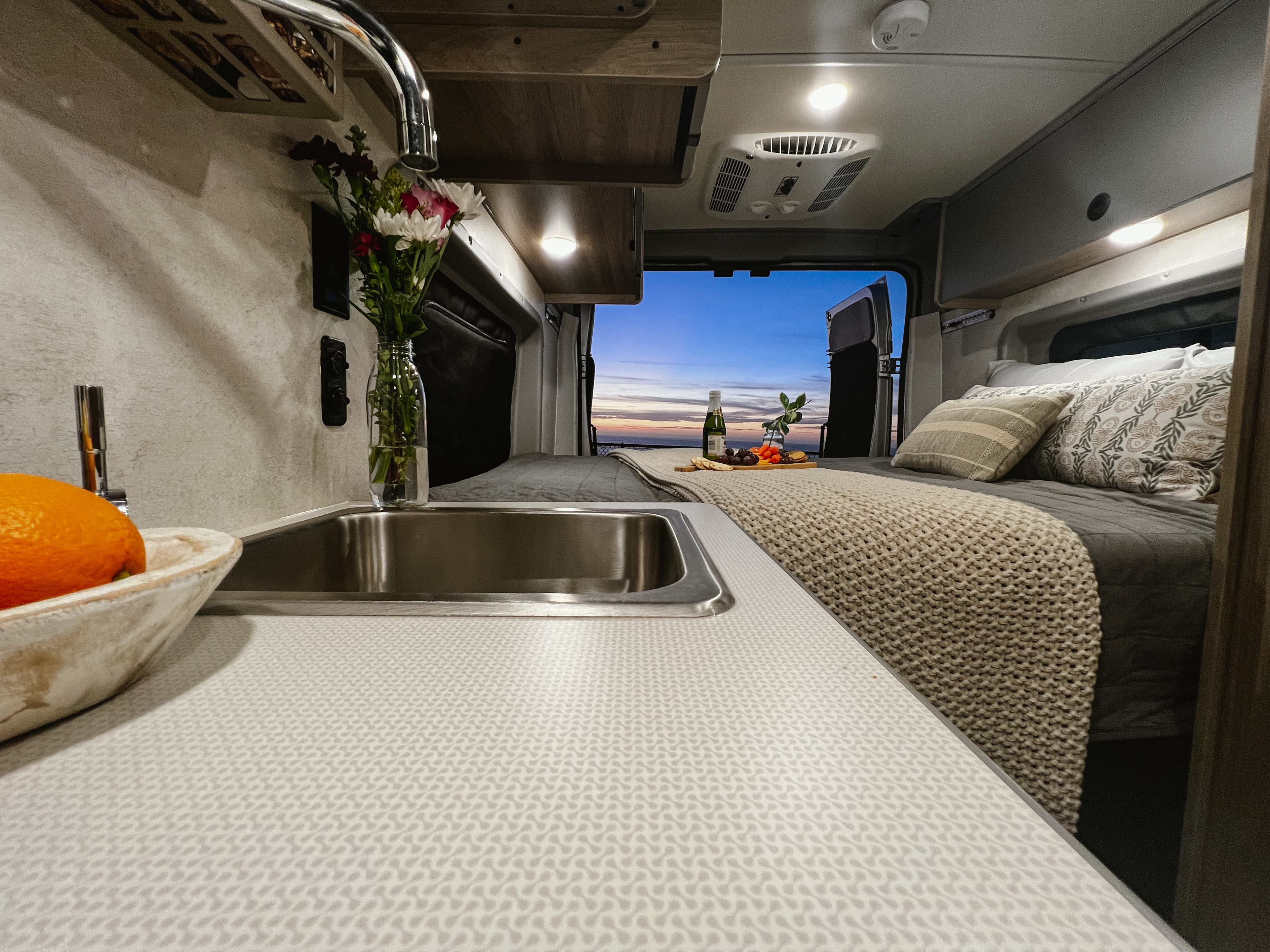 Experience comfort in this rv rental. Interior view of a well-equipped camper van with a kitchen, bed, and stunning ocean sunset.. Winnebago Solis 59PX 2023