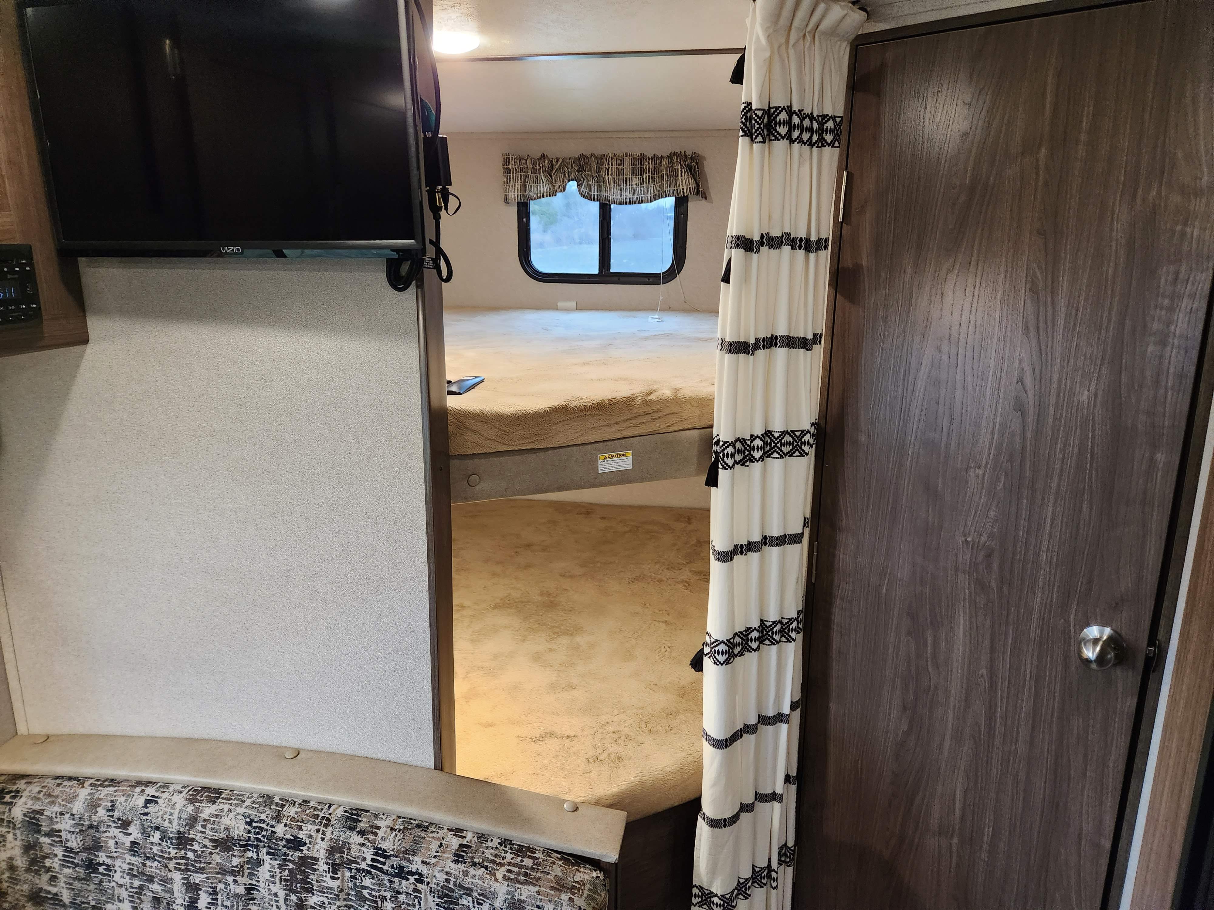An RV rental's cozy bunk bed area, complete with a mounted TV and decorative privacy curtain.. Keystone RV Hideout LHS 2019