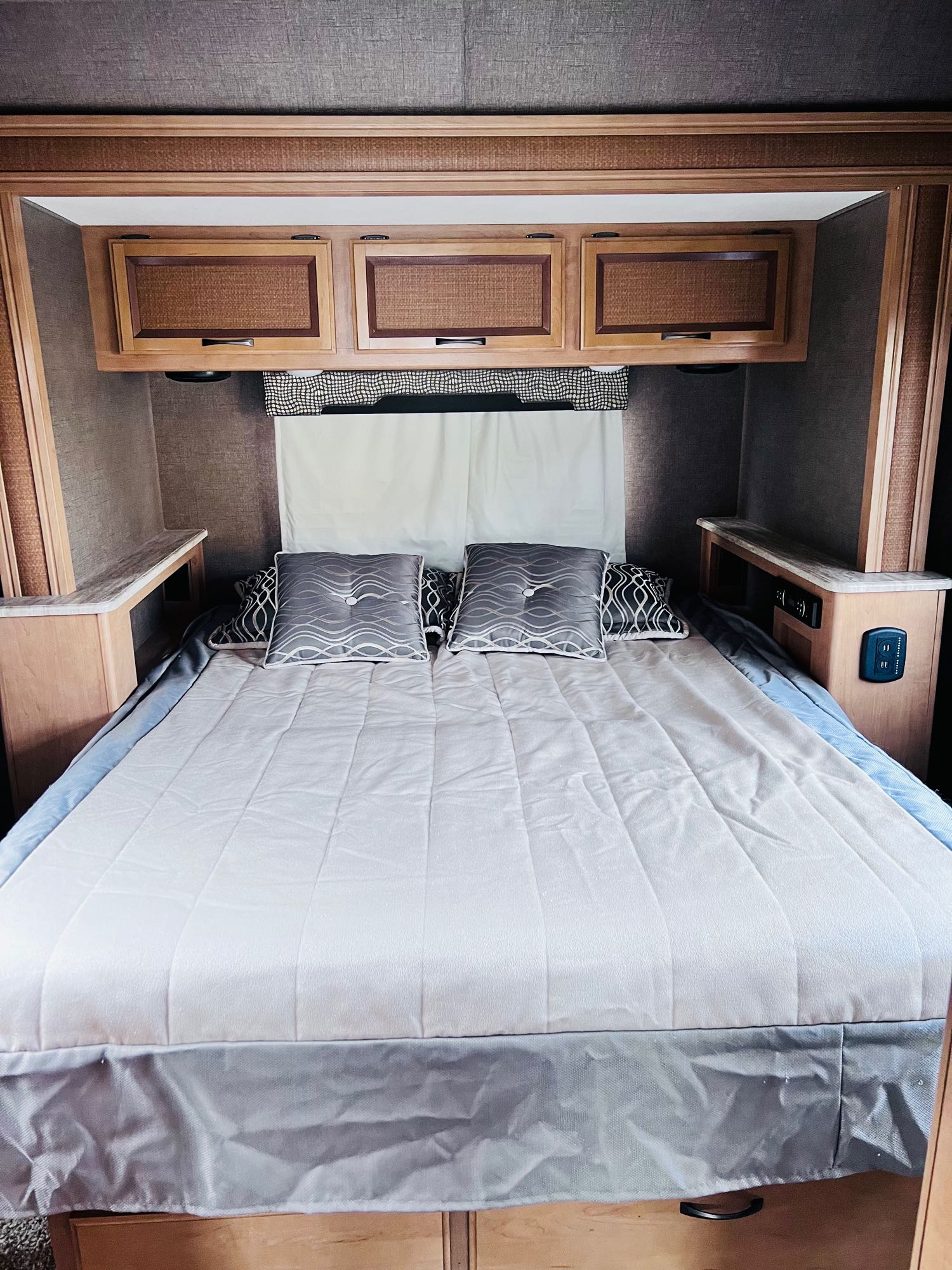 Cozy RV rental bedroom: queen bed with grey pillows, wood cabinets, and integrated nightstands with outlets.. Thor Vegas 2017