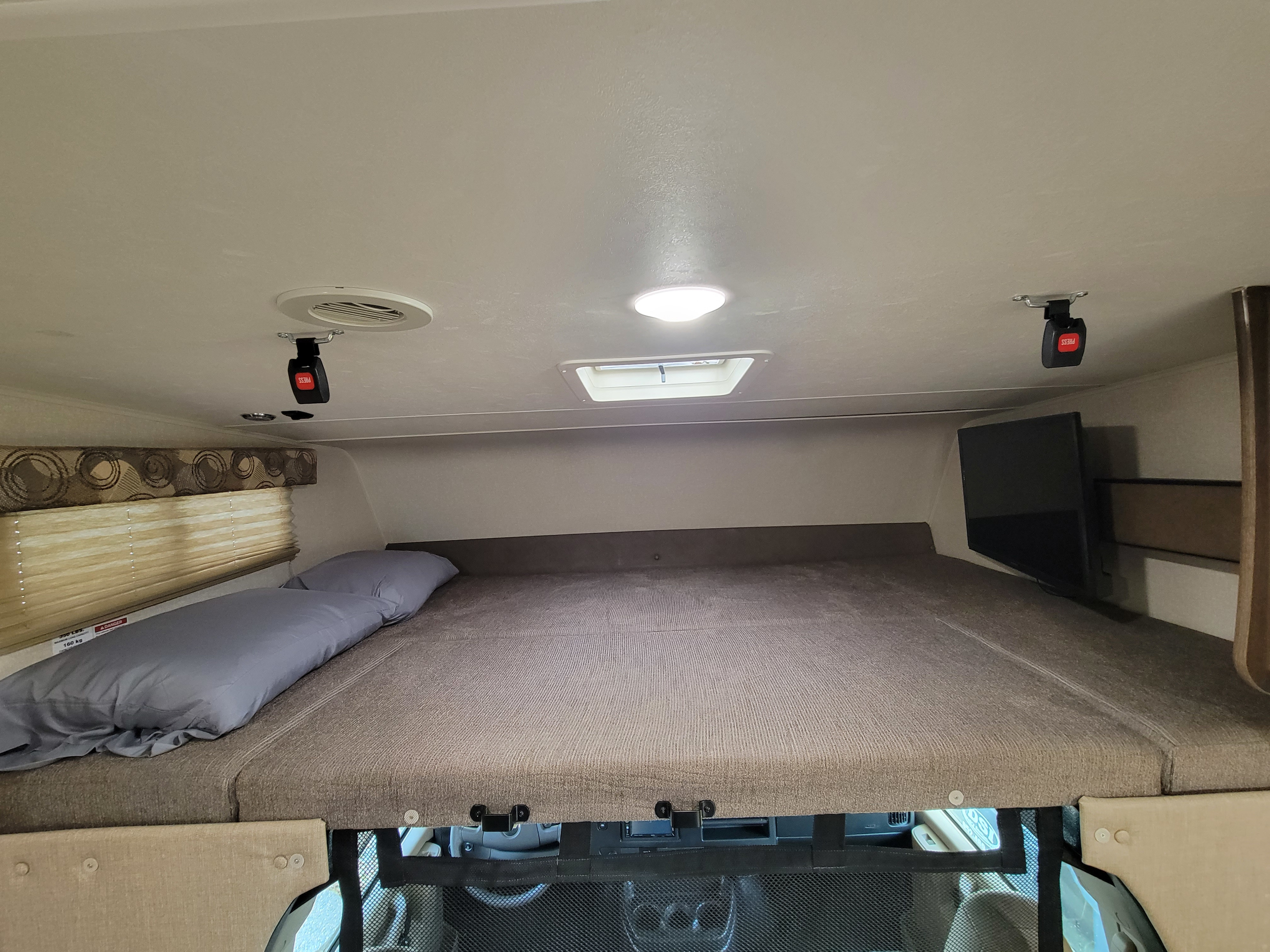 RV rental over-cab sleeping area: bed, pillow, TV, and window. Note the safety buckles and mesh netting.. Coachman Freelander 2019