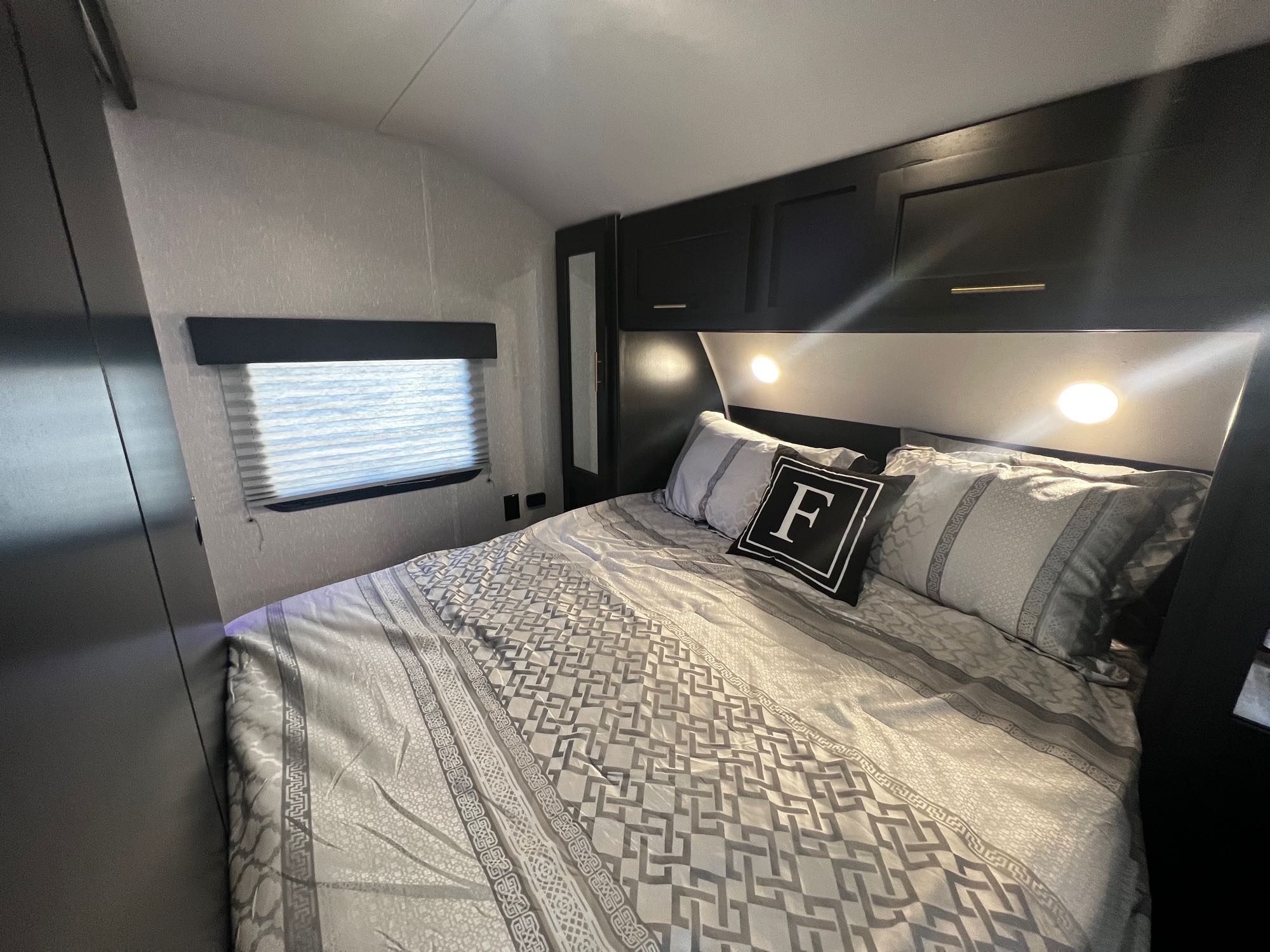 Cozy RV rental bedroom featuring patterned gray bedding, overhead storage, and warm lights. Ideal for a comfortable road trip.. Forest River Cherokee Grey Wolf 2022
