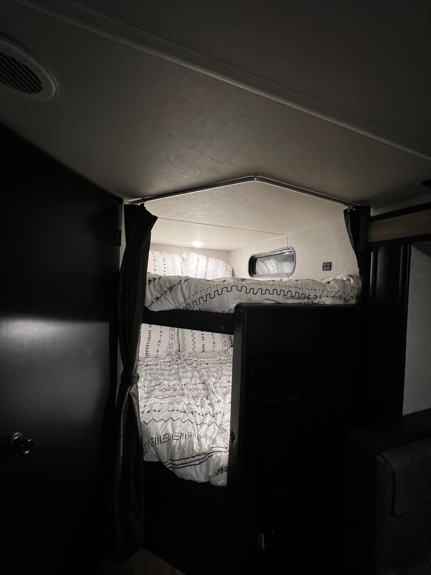 Cozy bunk beds in an RV rental, featuring white patterned bedding and a small window, create a compact sleeping area for a camper.. Forest River Cherokee Grey Wolf 2022