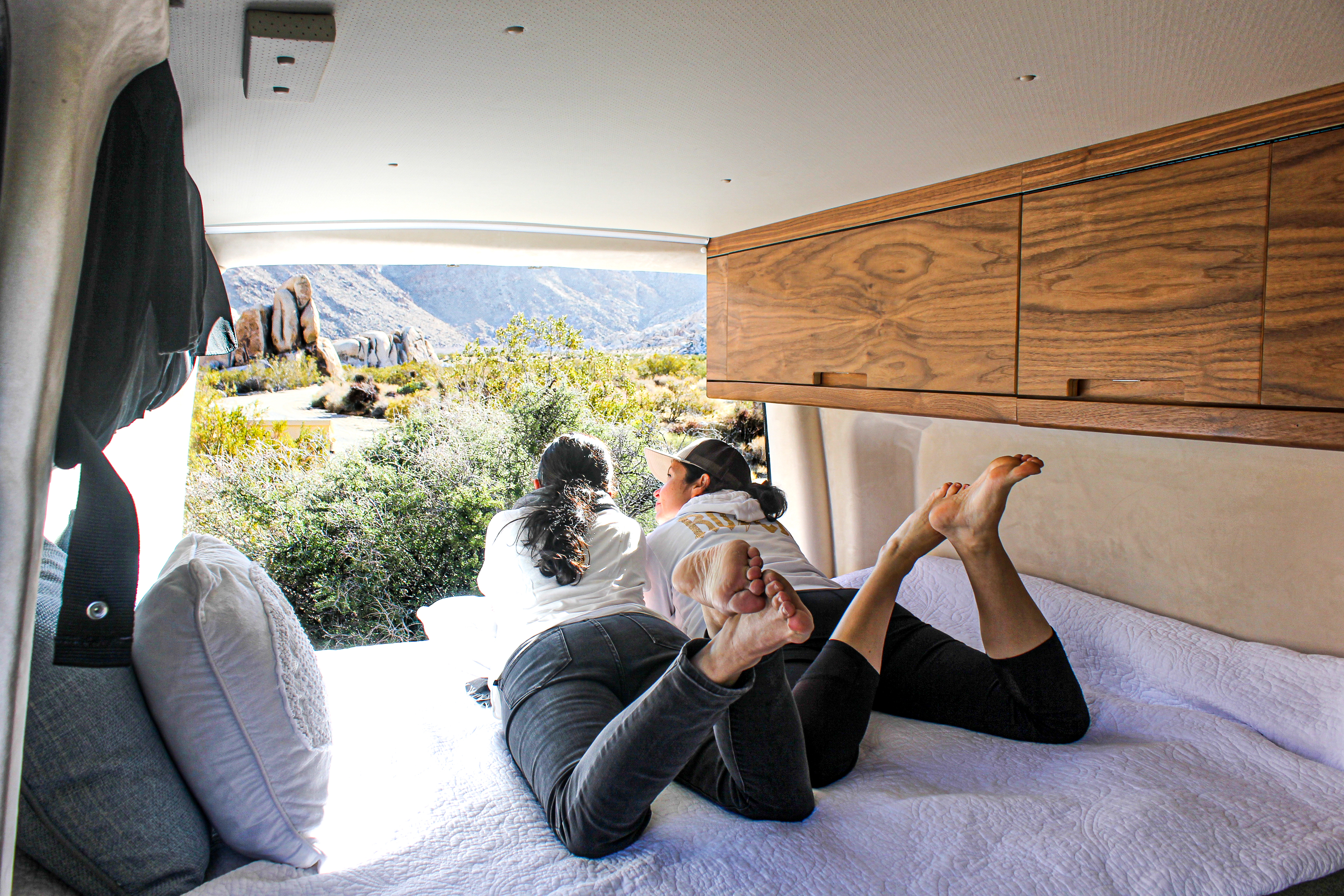 RV rental comfort: Two women relax in a camper van, enjoying desert mountain views from a cozy bed.. Mercedes-Benz texino 2020