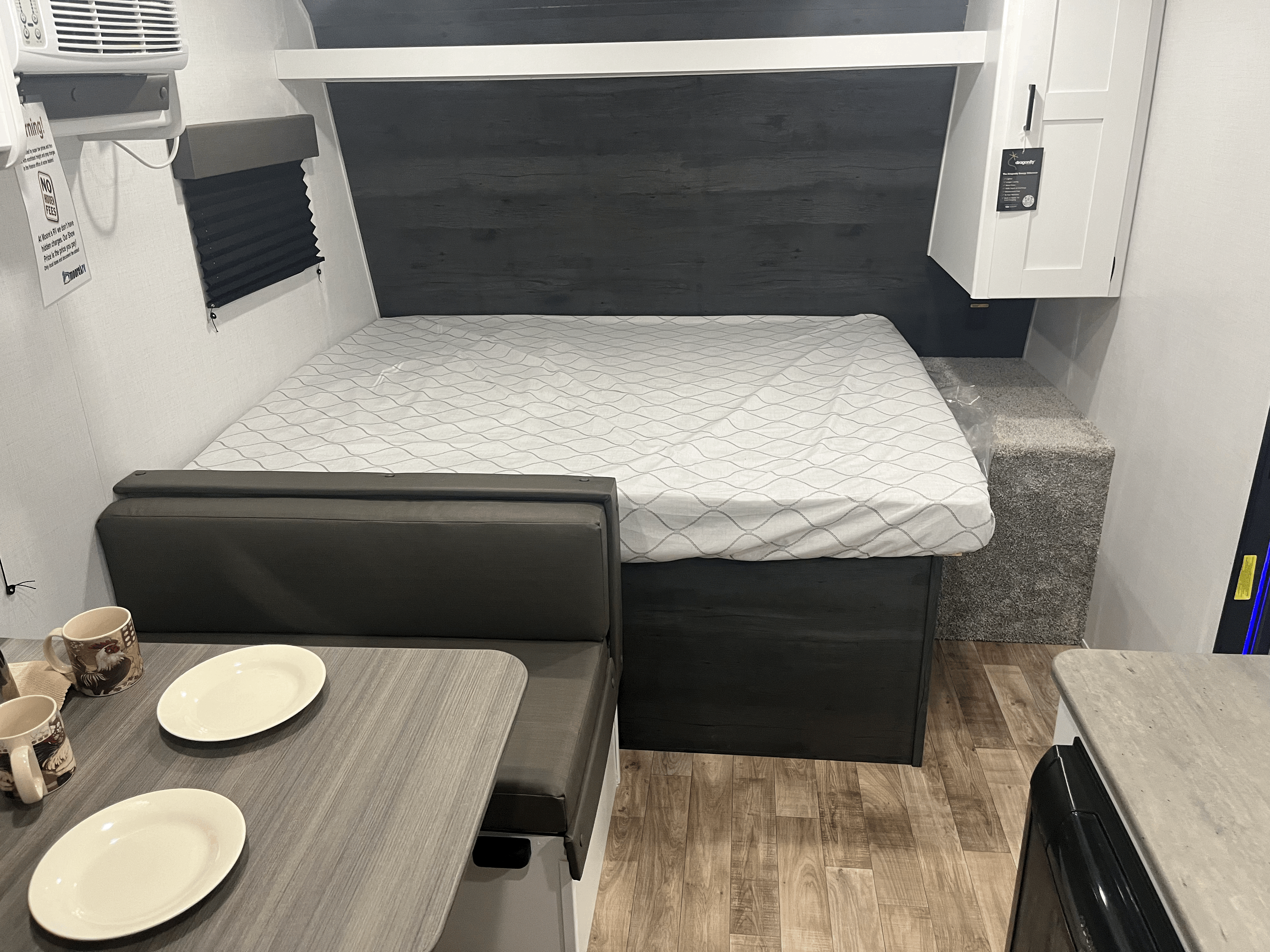 RV rental interior: a bed with patterned sheets, dark dinette seating, and overhead cabinets create a functional space.. Keystone RV Hideout 2022