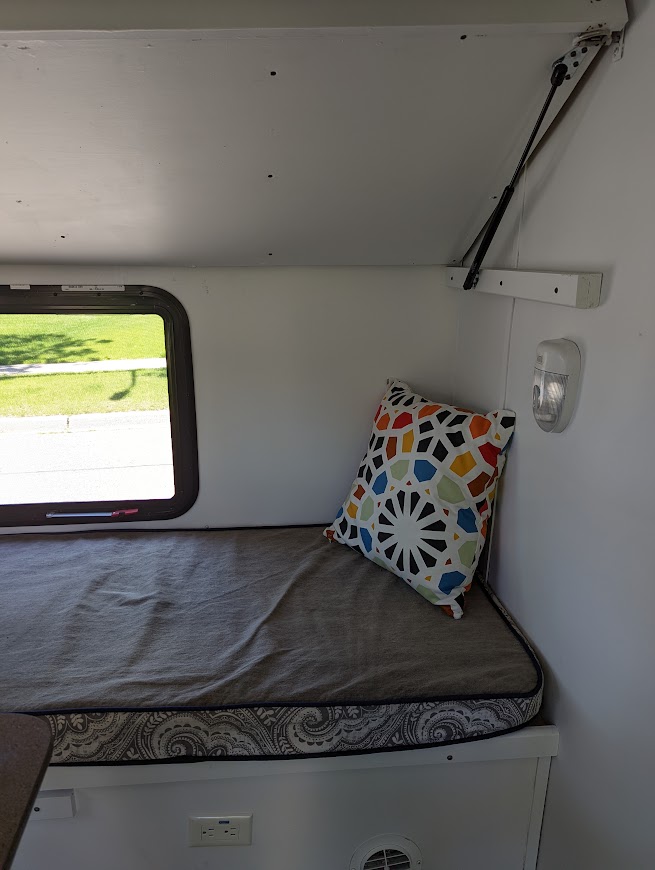RV rental interior: A cozy bench/bed with patterned cushion, colorful pillow, a window view, and overhead storage support.. Gulf Stream Vista Cruiser M-19RSD 2013